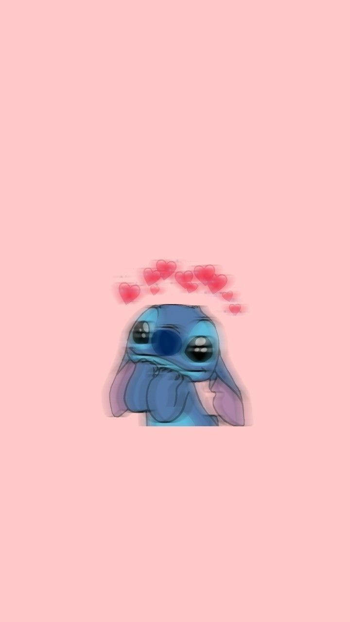 cute stitch iPhone 桌布 壁紙 — 一個可愛的藍色外星人，有大眼睛和粉紅色心形漂浮在頭頂，背景是柔和的粉紅色。