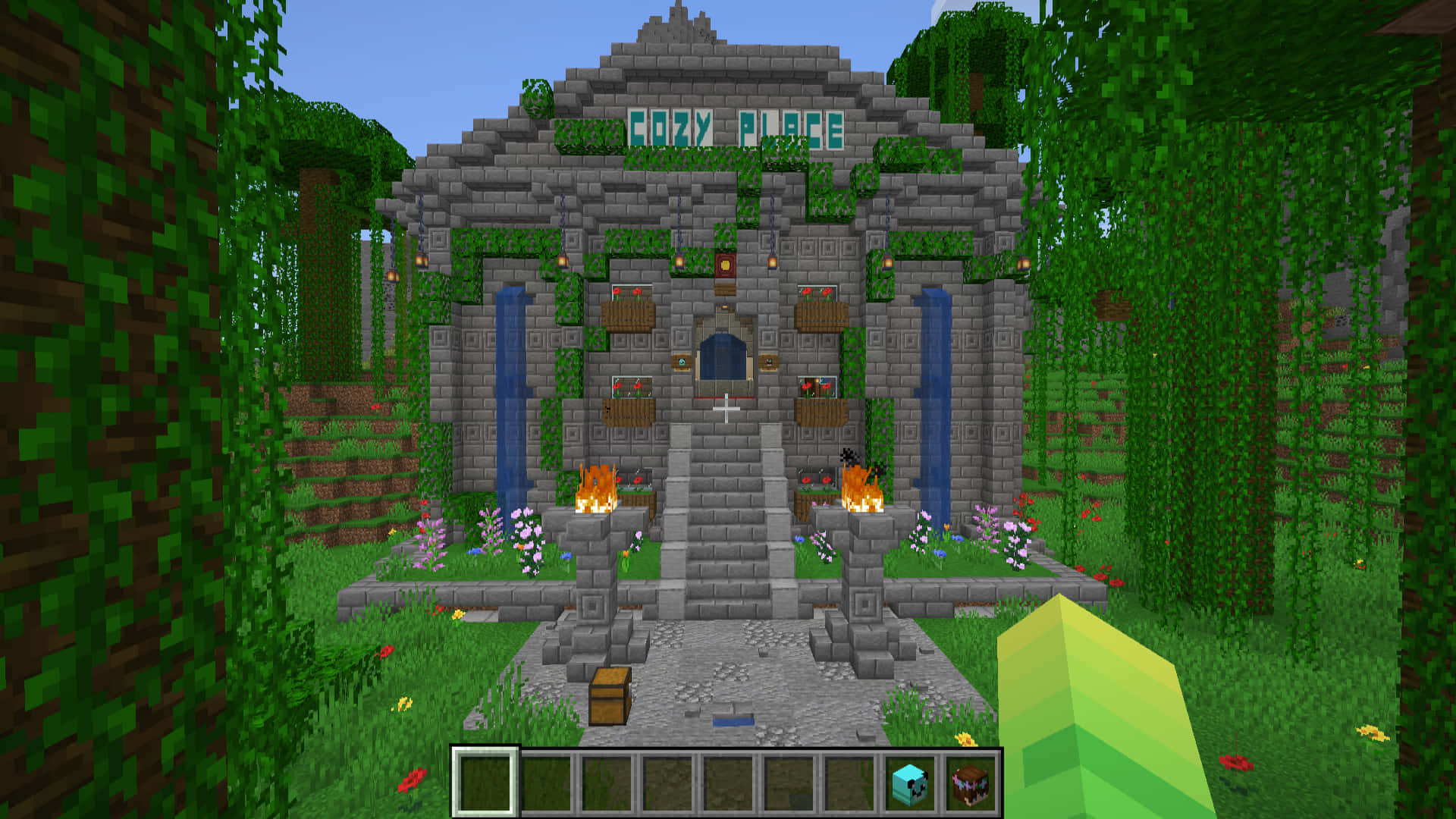 Minecraft Server 桌布 壁紙 — 一個名為「Cozy Place」的像素化 Minecraft 石屋，坐落在茂密的綠色森林中，配有火把和花朵。