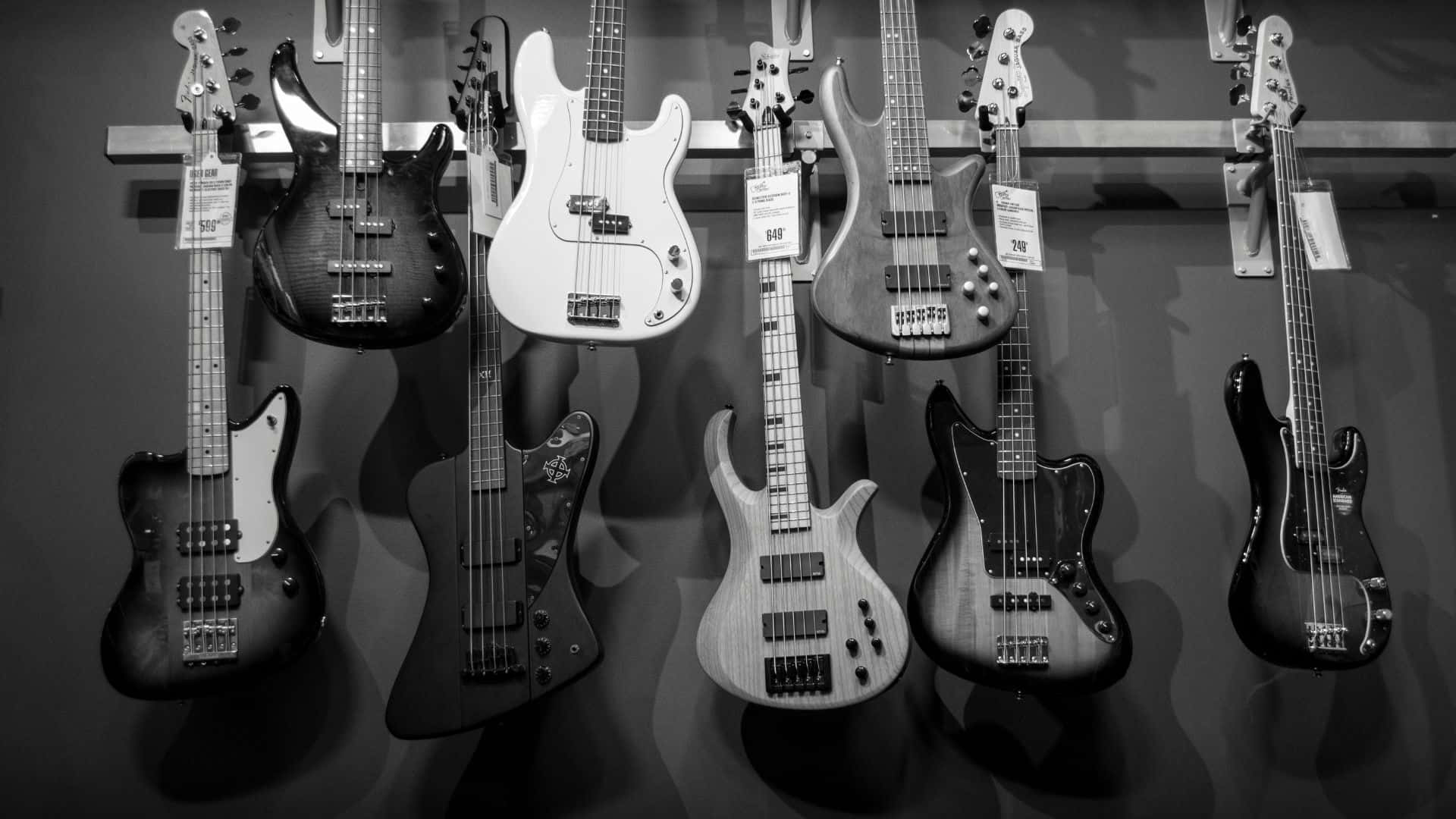 Black And White Guitar 桌布 壁紙 — 一個單色展示，各種低音結他整齊地掛在音樂店的牆上。