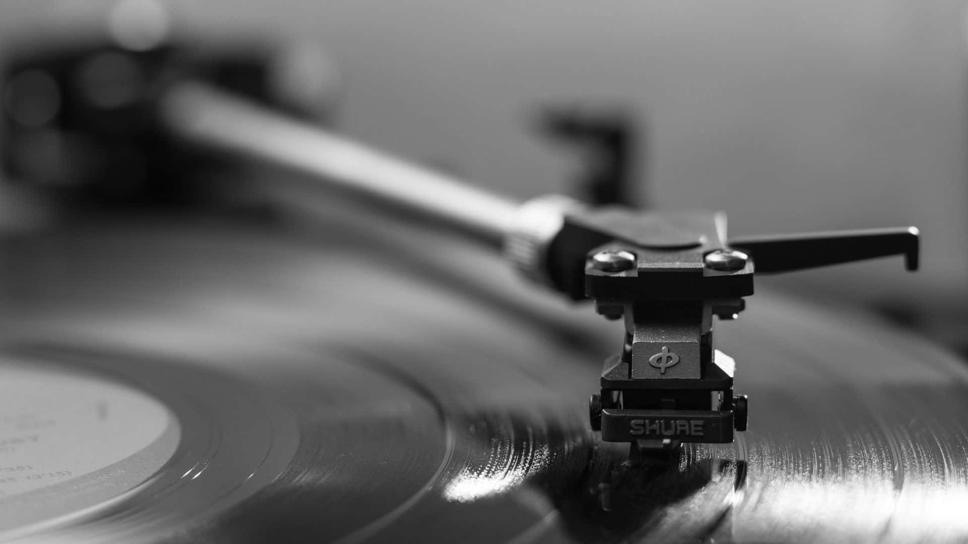 Black And White Music 桌布 壁紙 — 一個單色特寫，顯示Shure唱頭輕輕擱在旋轉的黑膠唱片坑紋上。