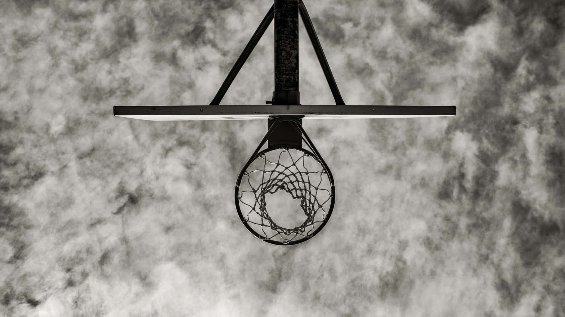 Cool Basketball 桌布 壁紙 — 一個單色籃球框懸掛在從下方觀看的戲劇性多雲天空前。