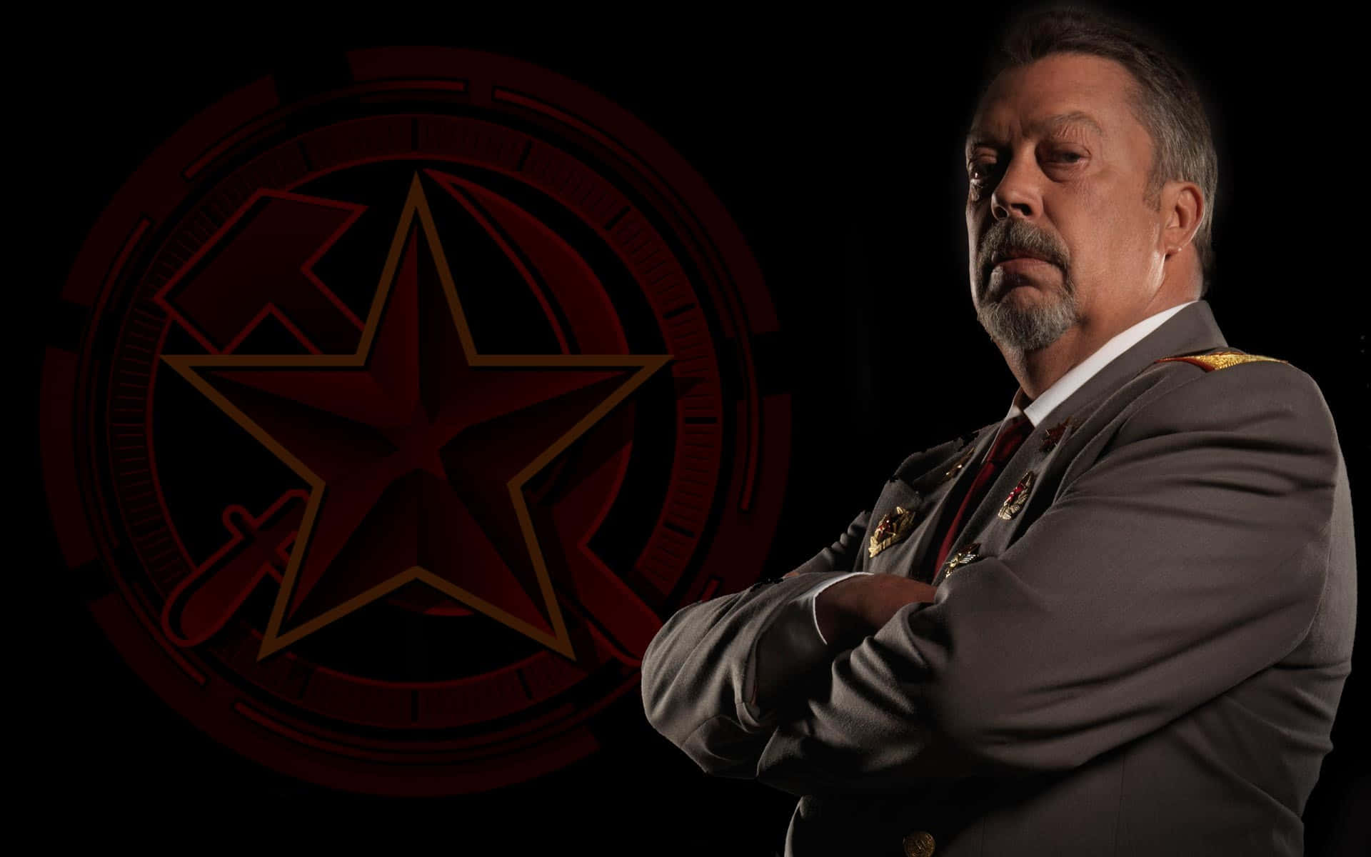 Tim Curry 桌布 壁紙 — 一個嚴肅嘅男人著住軍服，雙手交叉企喺一個黑暗背景前面，背景有一個發光嘅紅色星星標誌。