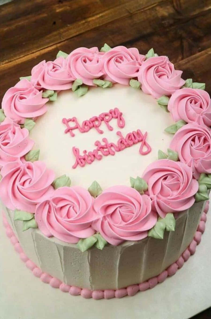 生日蛋糕 桌布 壁紙 — 一個圓形生日蛋糕，飾有粉紅色玫瑰擠花糖霜和綠色葉子，並用粉紅色糖霜寫上「Happy Birthday」。