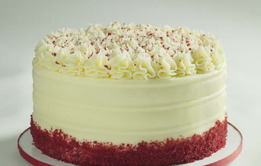 Red Velvet Cake 桌布 壁紙 — 一個圓形的紅絲絨蛋糕，帶有奶油白色糖霜和紅色碎屑配料，優雅地放在紅色蛋糕架上。
