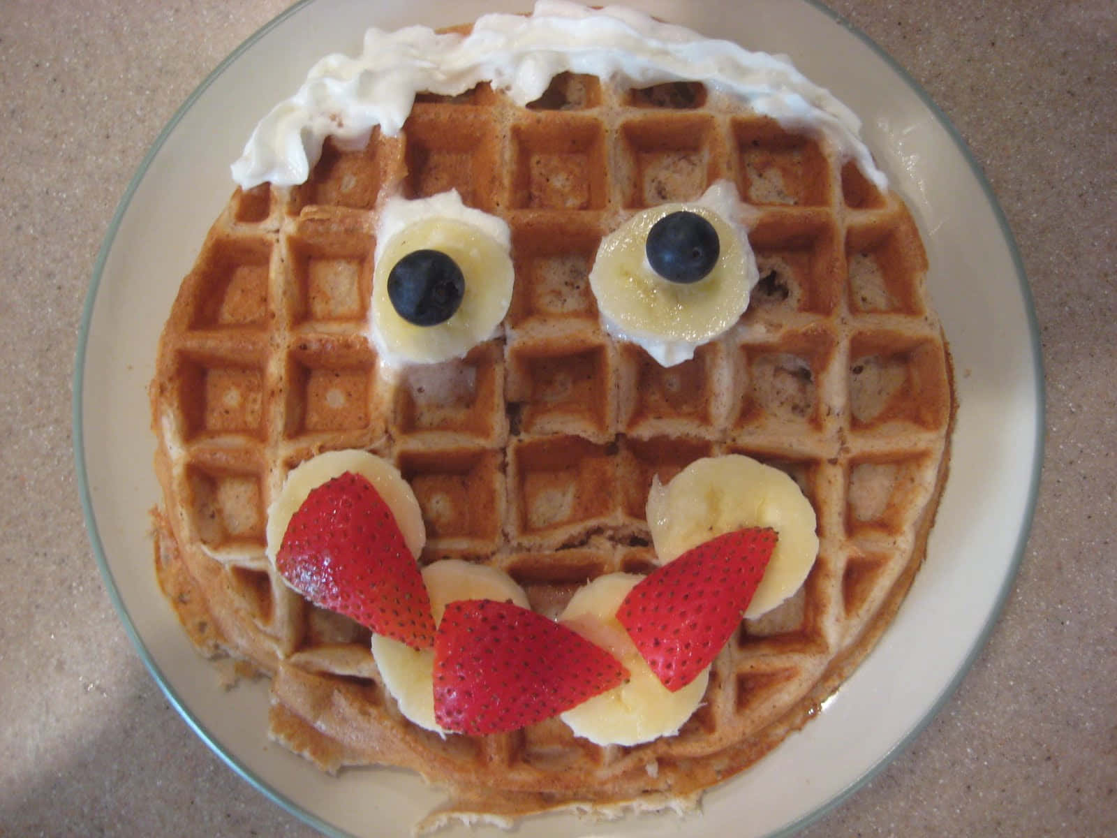 Waffle 桌布 壁紙 — 一個圓形窩夫，飾以忌廉、藍莓、香蕉片和草莓，形成一個歡樂的笑臉。