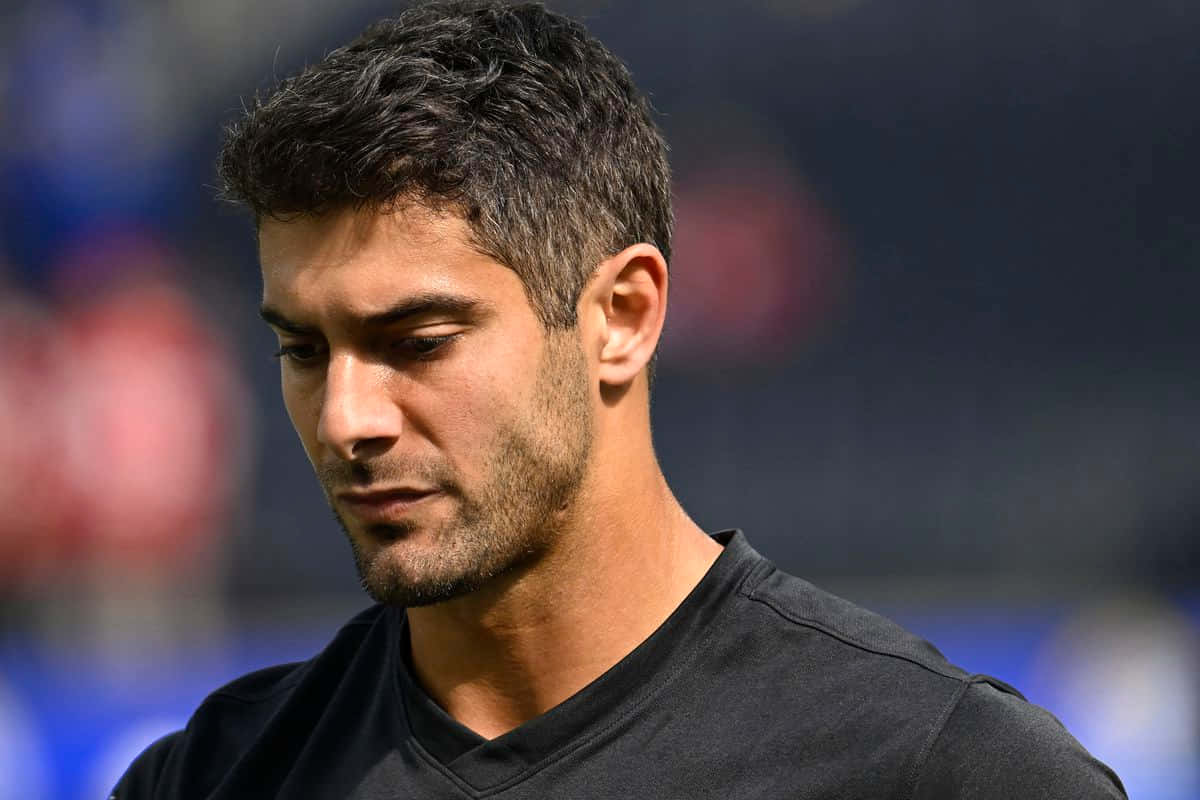 Jimmy Garoppolo 桌布 壁紙 — 一個在體育場環境中向下看的深色頭髮和鬍渣男人的特寫肖像。