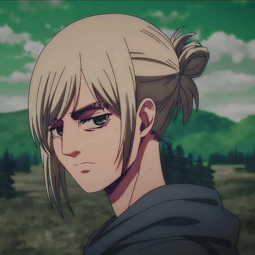 Annie Leonhart 桌布 壁紙 — 一個堅定的動漫女孩，金色頭髮向後紮起，在綠色山丘和多雲天空的背景下專注地凝視。