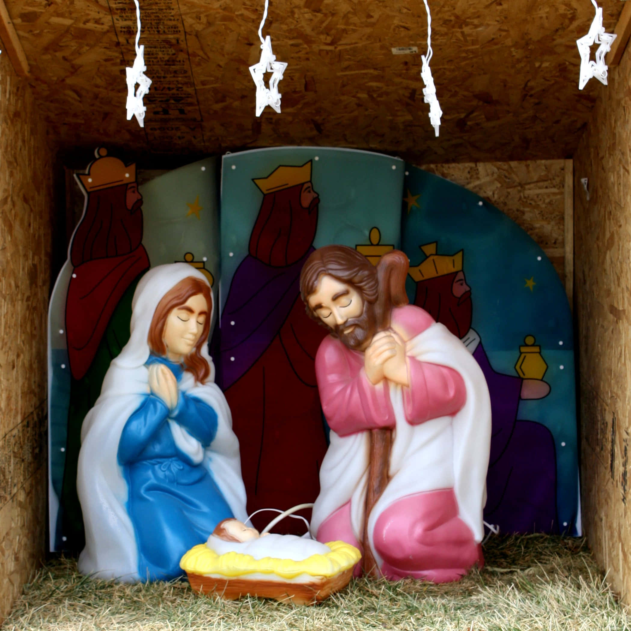 Nativity 桌布 壁紙 — 一個塑膠耶穌誕生場景，瑪利亞和約瑟跪在馬槽裏的嬰兒耶穌旁邊，上方懸掛著星星裝飾。