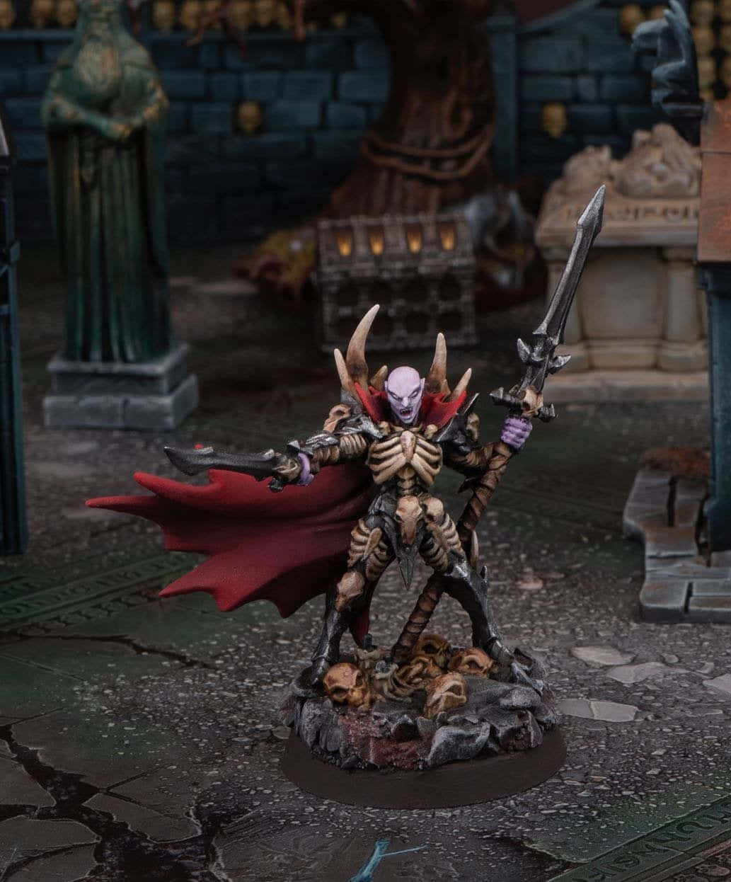 Vampire Lord 桌布 壁紙 — 一個塗漆的迷你骷髏戰士，有角和紅色斗篷，站在頭骨底座上，在黑暗的石庭院中手持劍。