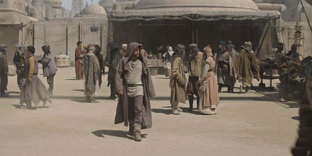 Mos Eisley 桌布 壁紙 — 一個塵土飛揚的沙漠市集，在明亮的日光下，圓頂結構下擠滿了身穿長袍的人物。