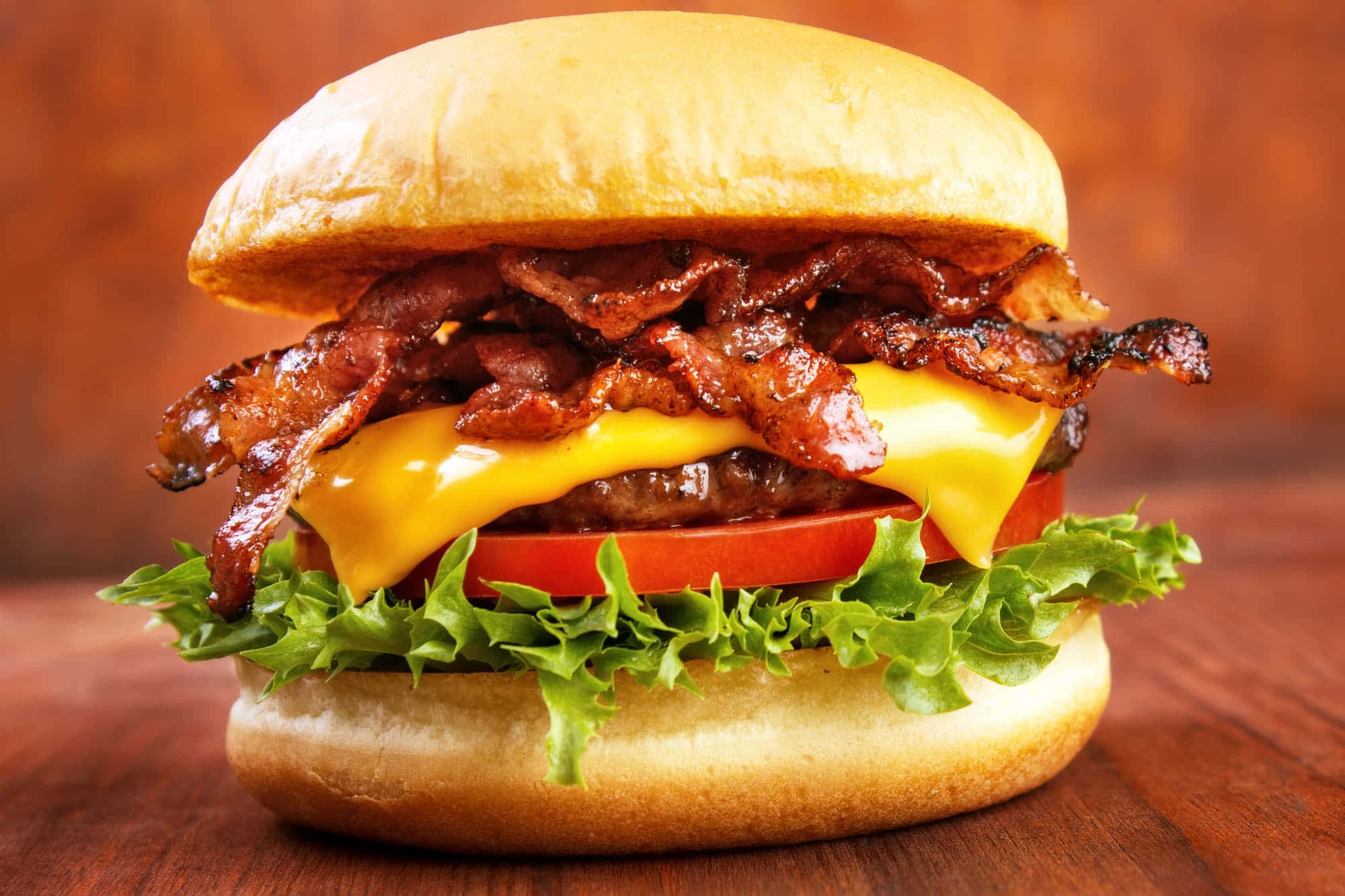bacon 桌布 壁紙 — 一個多汁的漢堡，配上脆煙肉、融化芝士、番茄和生菜，放在木質表面上。