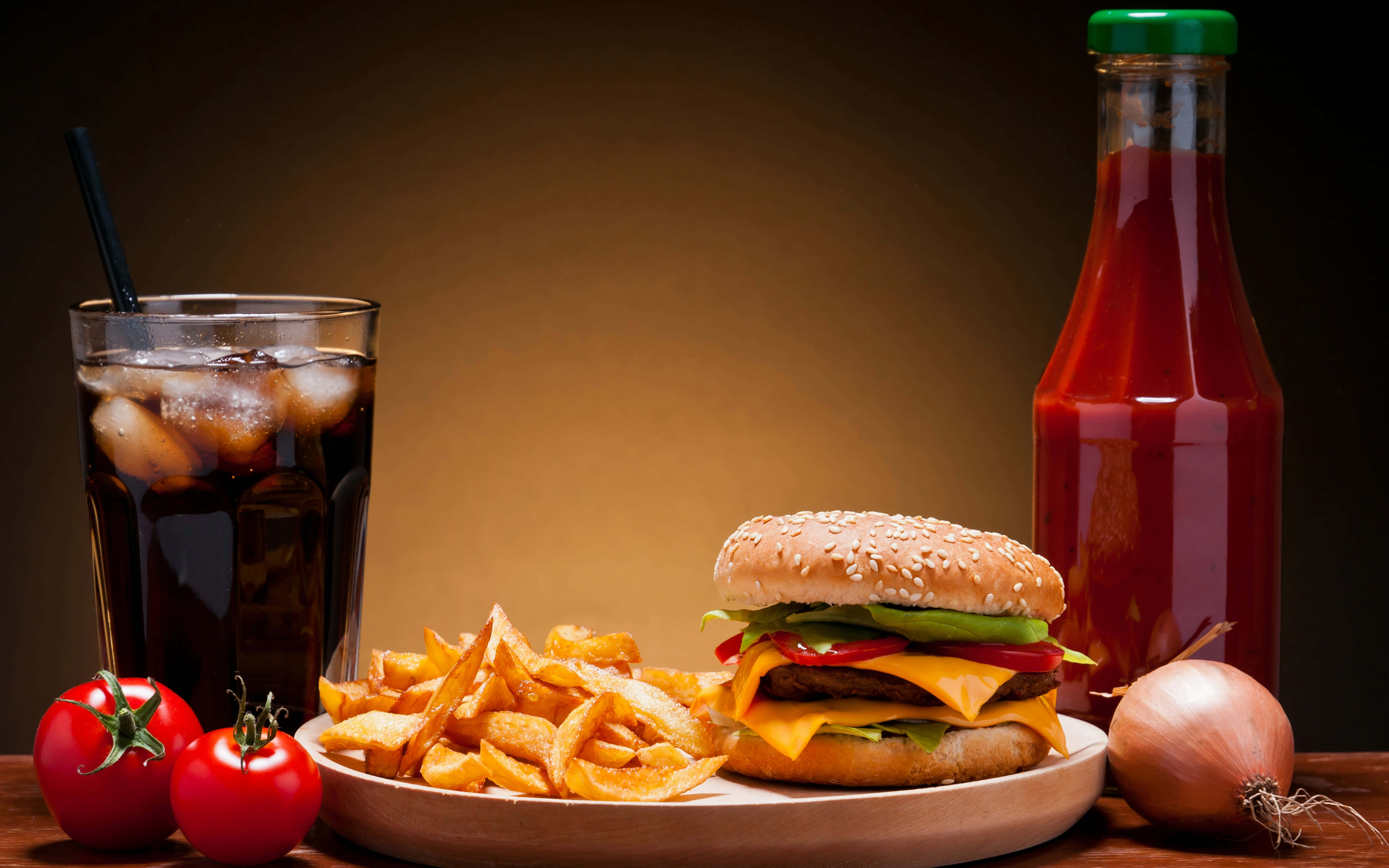 Food And Beverage 桌布 壁紙 — 一個多汁的芝士漢堡配薯條和一杯可樂，旁邊有茄汁樽和新鮮番茄在木桌上。