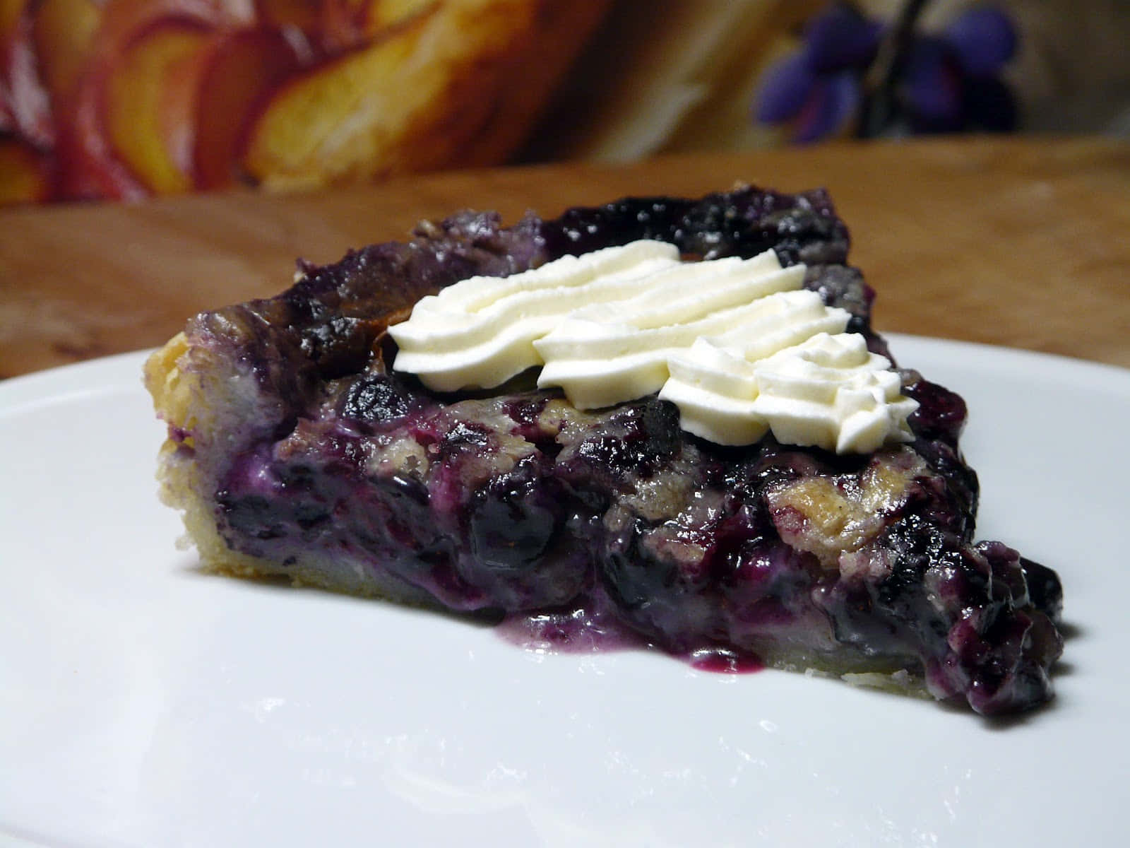 Blueberries Tart 桌布 壁紙 — 一個多汁藍莓批切片嘅特寫，上面有唧花忌廉，放喺白色碟上。
