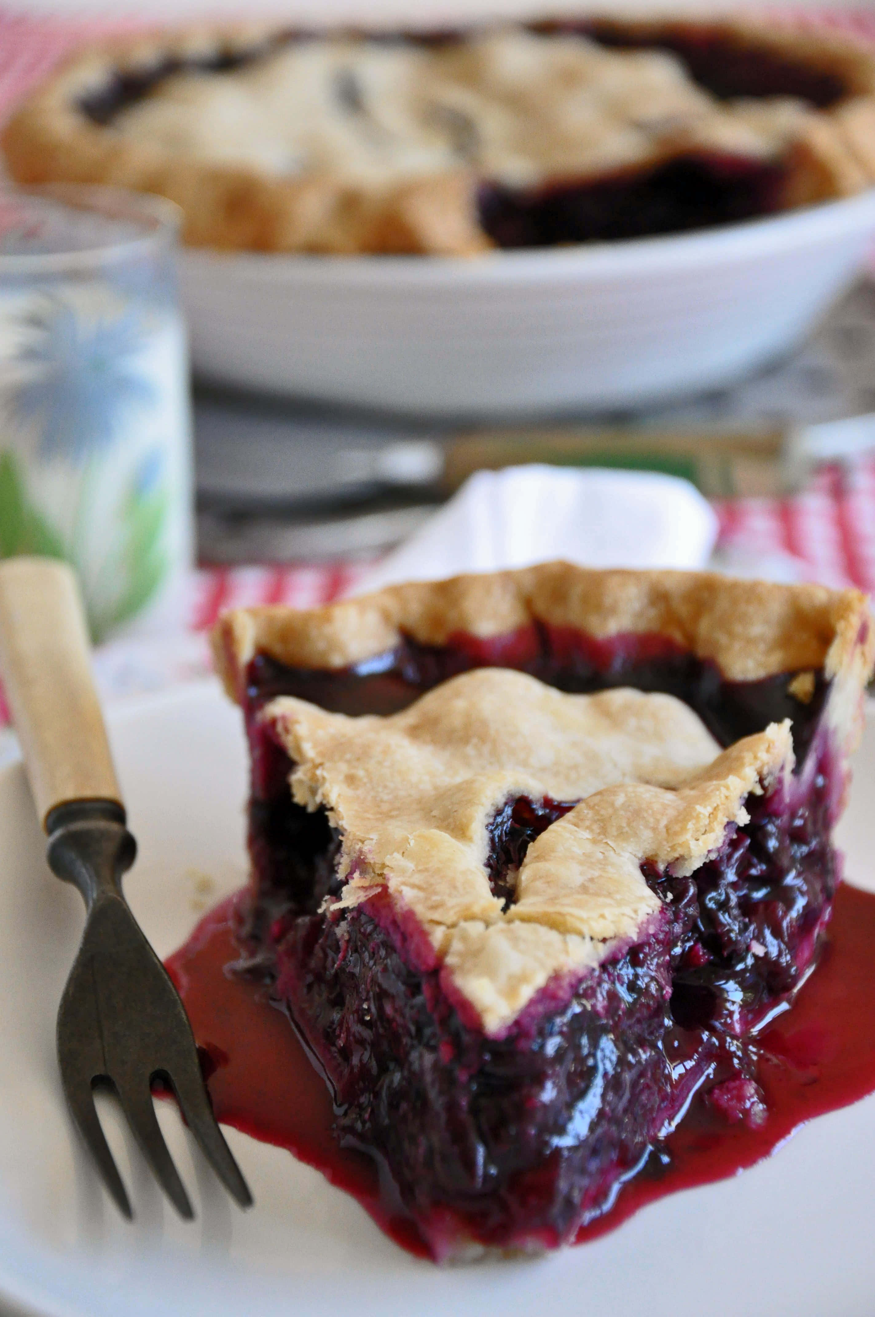 Blueberry Pie 桌布 壁紙 — 一個多汁藍莓批的近鏡，金黃色批皮配上糖漿餡料，放在白色碟上。