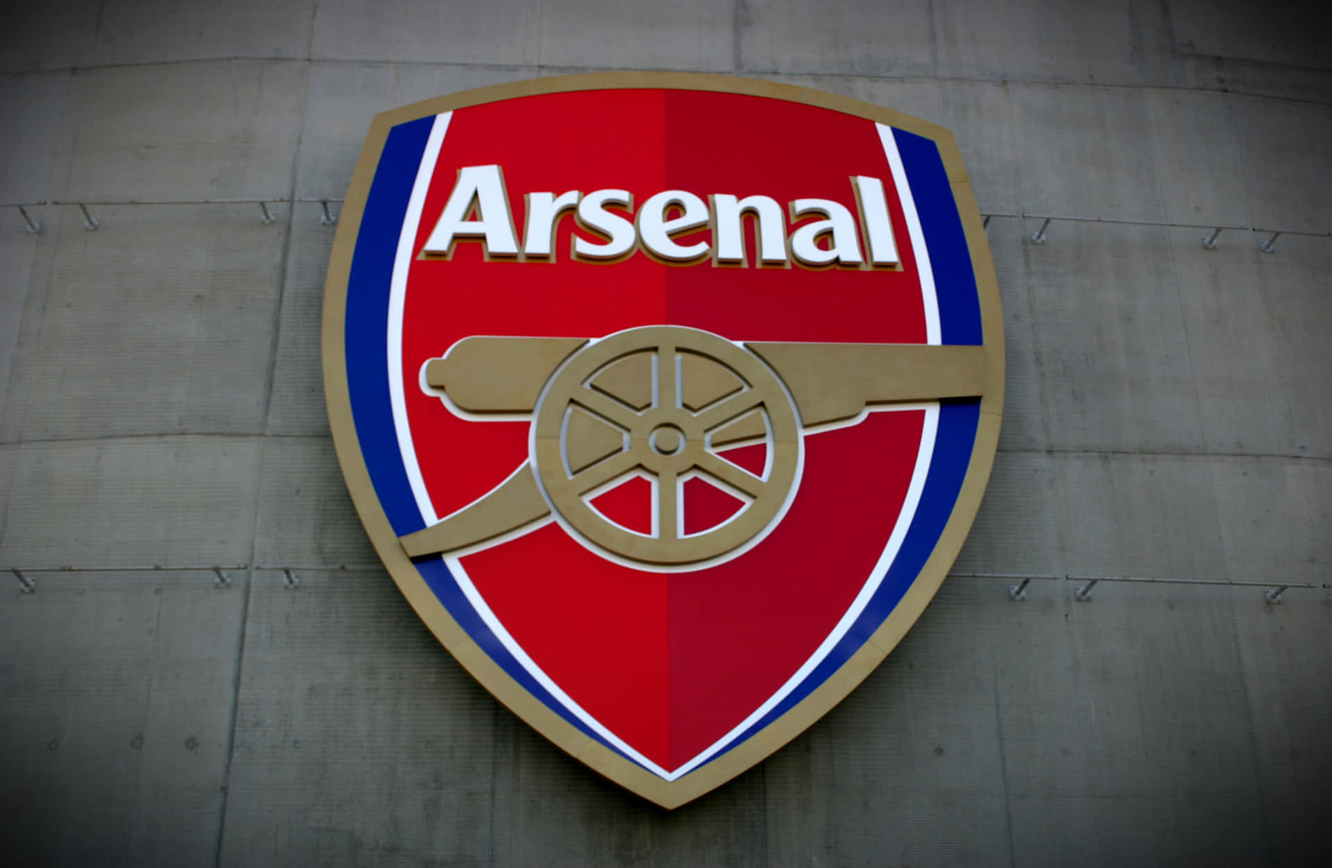 Arsenal 桌布 壁紙 — 一個大型立體阿仙奴足球會徽章安裝在混凝土牆上，採用大膽的紅、藍和金色。