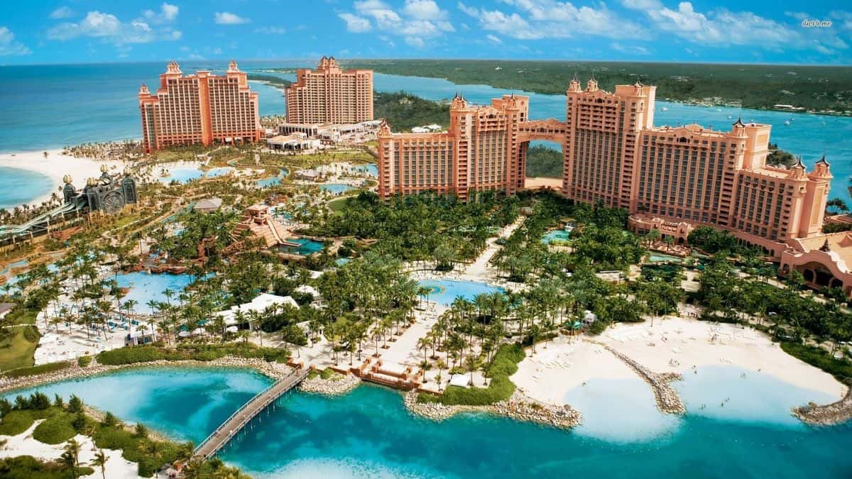 Bahamas Island 桌布 壁紙 — 一個大型粉紅色度假村綜合體的鳥瞰圖，擁有碧綠的海水、白色沙灘和茂密的綠植，在明亮的藍天下。
