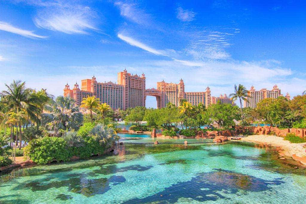 Bahamas Island 桌布 壁紙 — 一個大型豪華度假村，擁有粉紅色塔樓和茂密的棕櫚樹，俯瞰著碧綠的海水，上方是明亮的藍天。