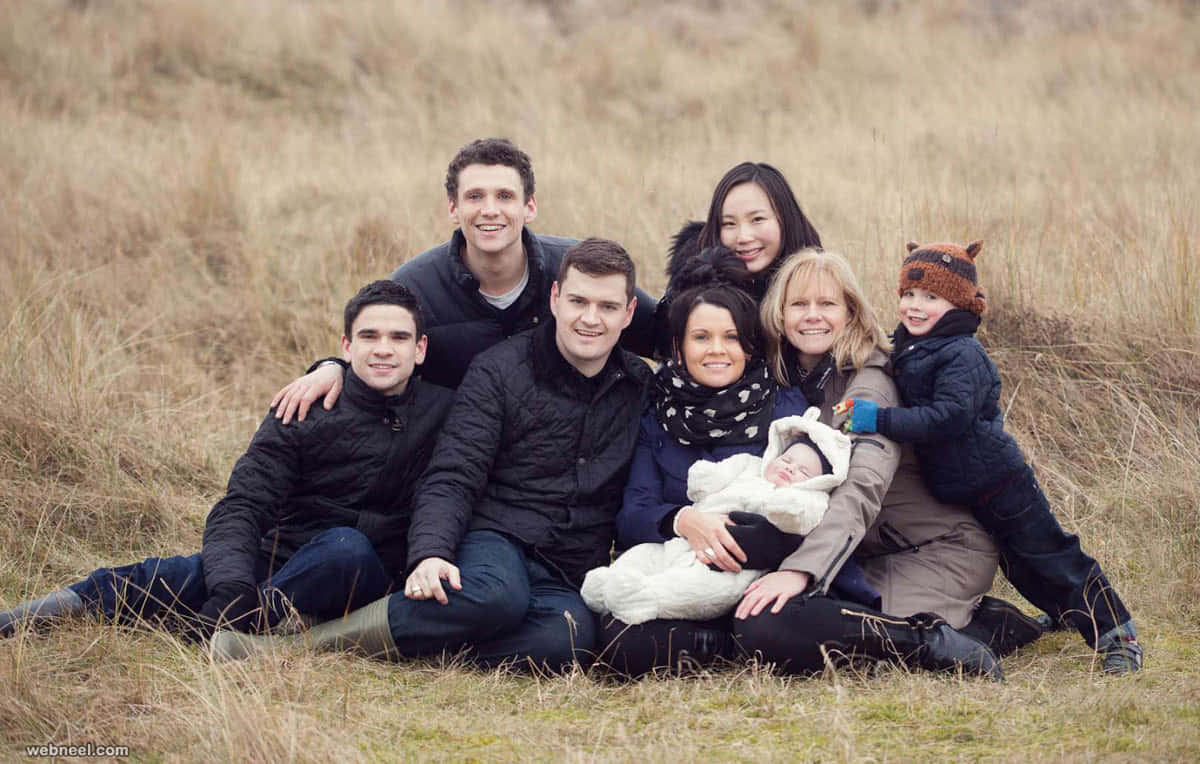 Family Portrait 桌布 壁紙 — 一個大家庭面帶微笑，穿著冬季外套和帽子，在乾草地上一起擺姿勢。