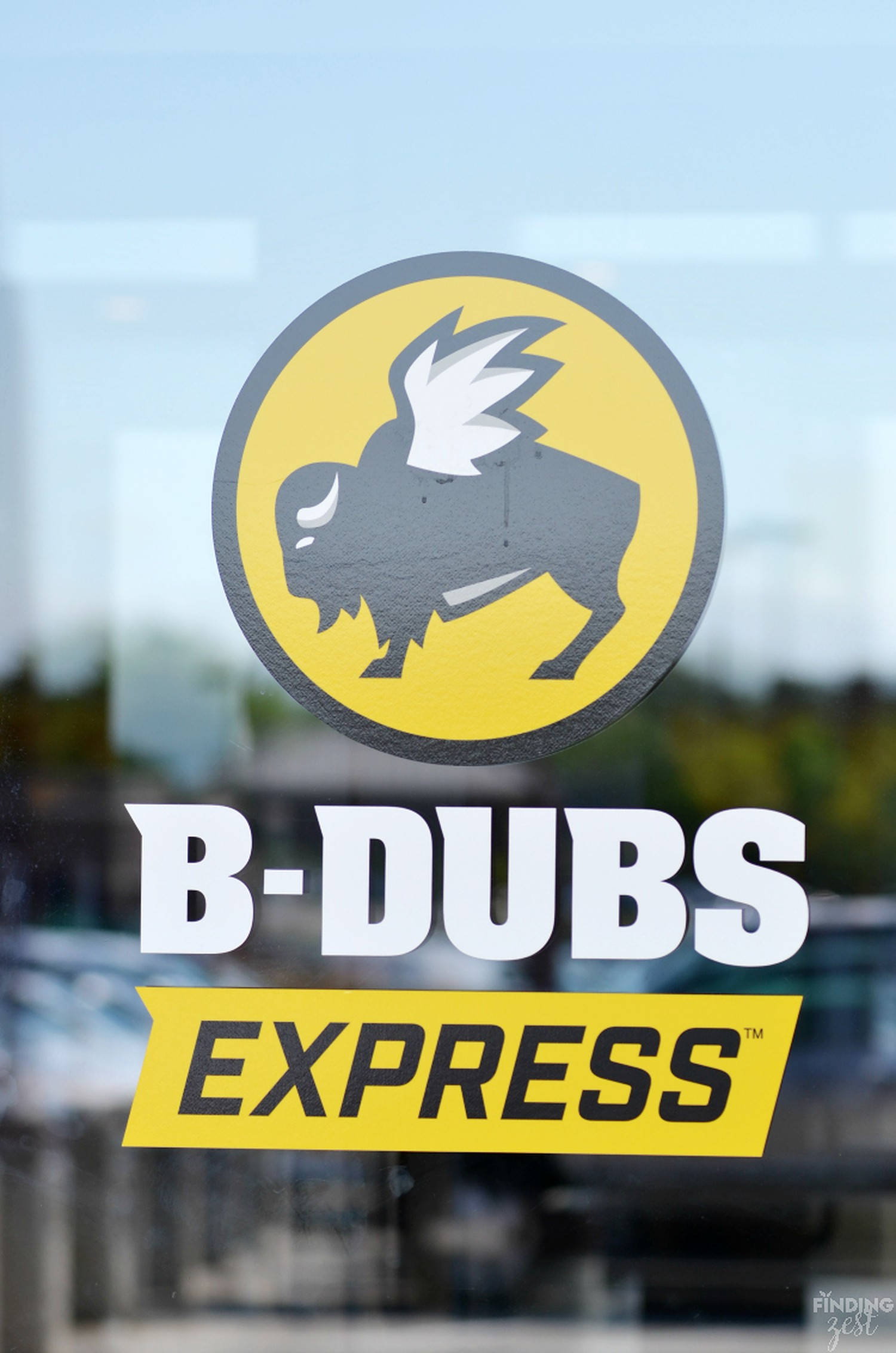 Buffalo Wild Wings B-Dubs Express 壁紙 — 一個大膽的黃色和灰色帶翅膀的水牛標誌，位於玻璃店面櫥窗上，下方有 'B-DUBS EXPRESS' 文字。