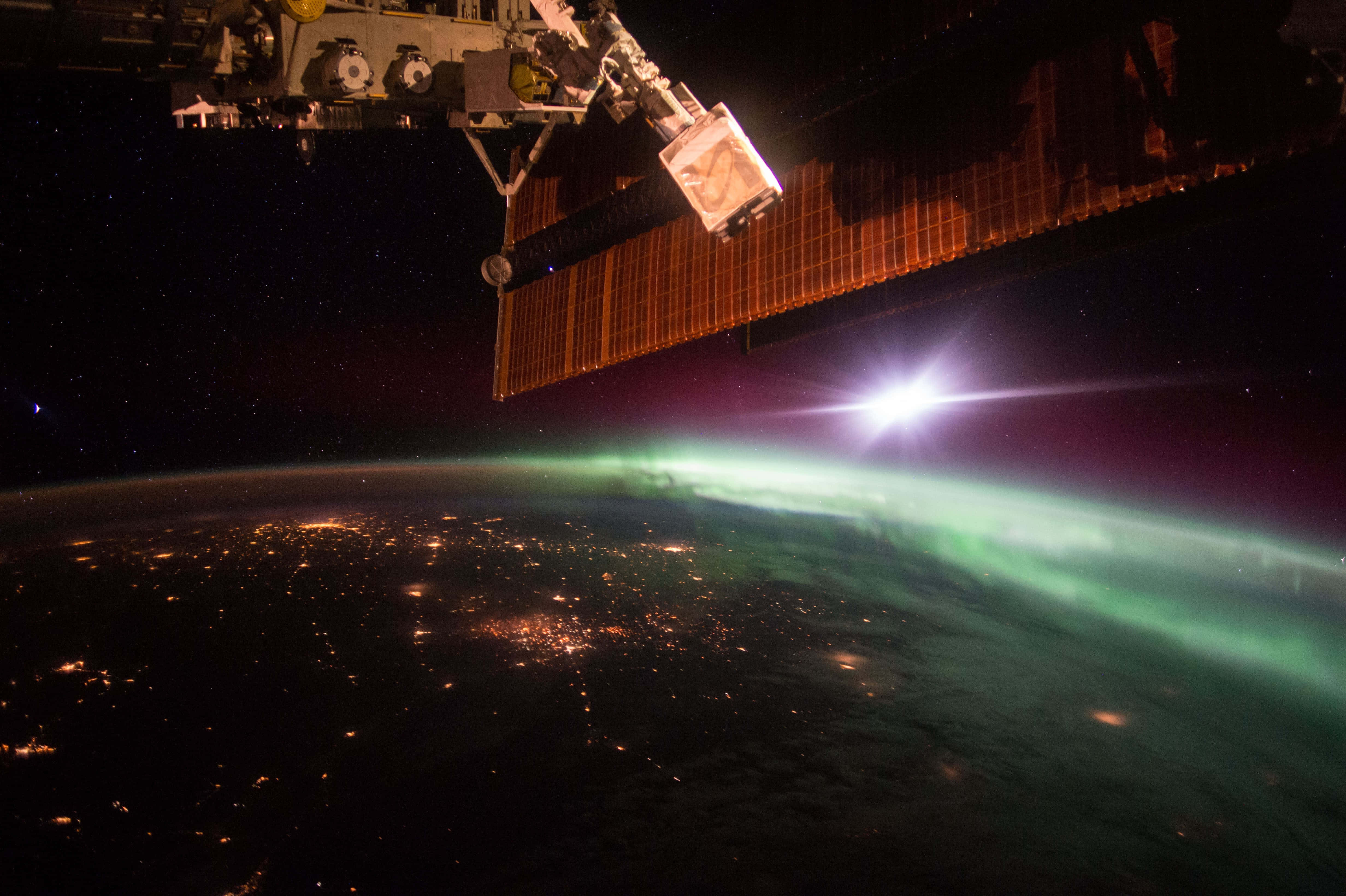 Iss 桌布 壁紙 — 一個太空站在夜間懸浮在地球上空，下方有城市燈光和發光的極光。