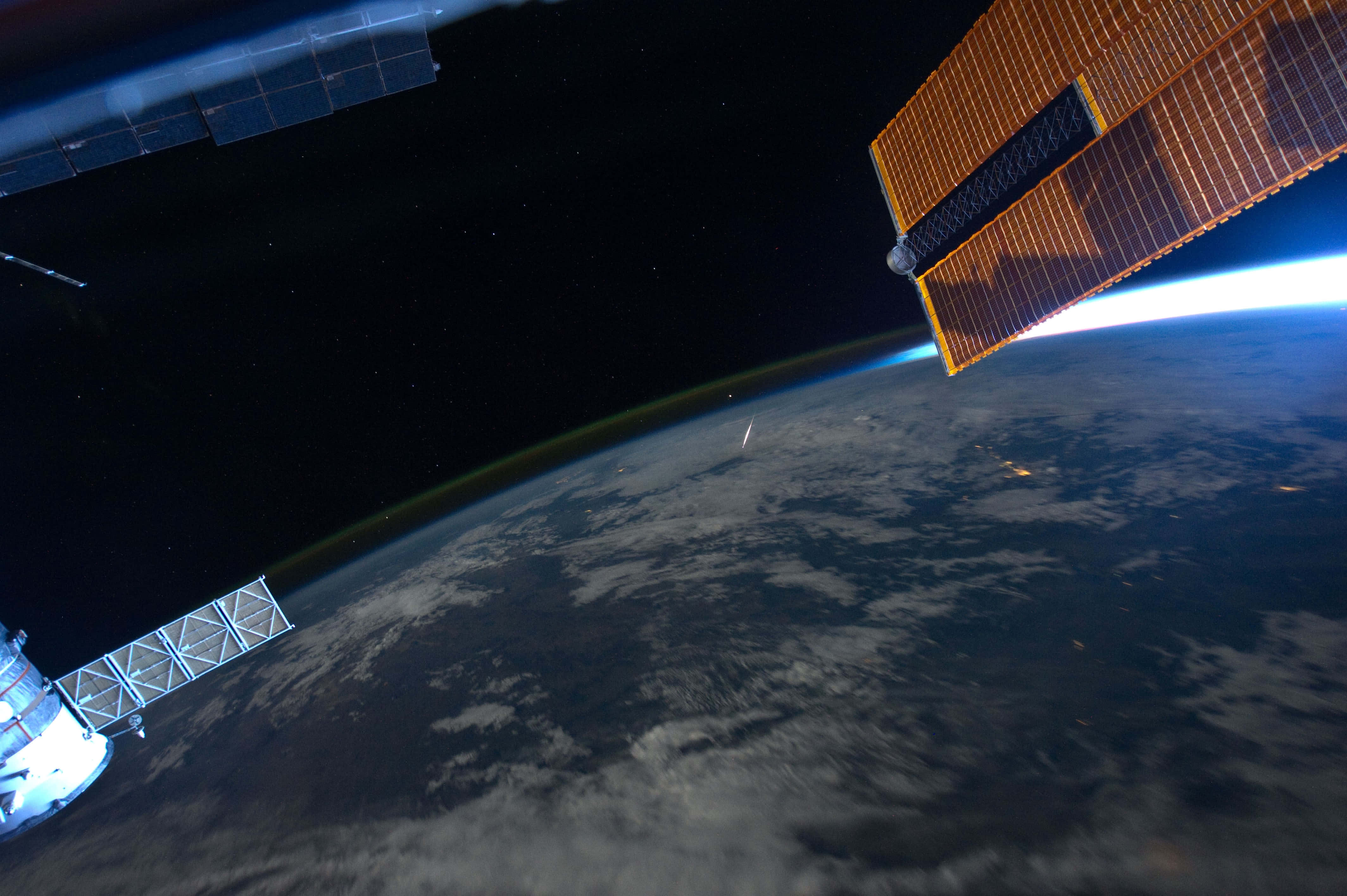 Iss 桌布 壁紙 — 一個太空站繞地球運行，太陽能板在太空的漆黑中發光，下方是行星彎曲的地平線。