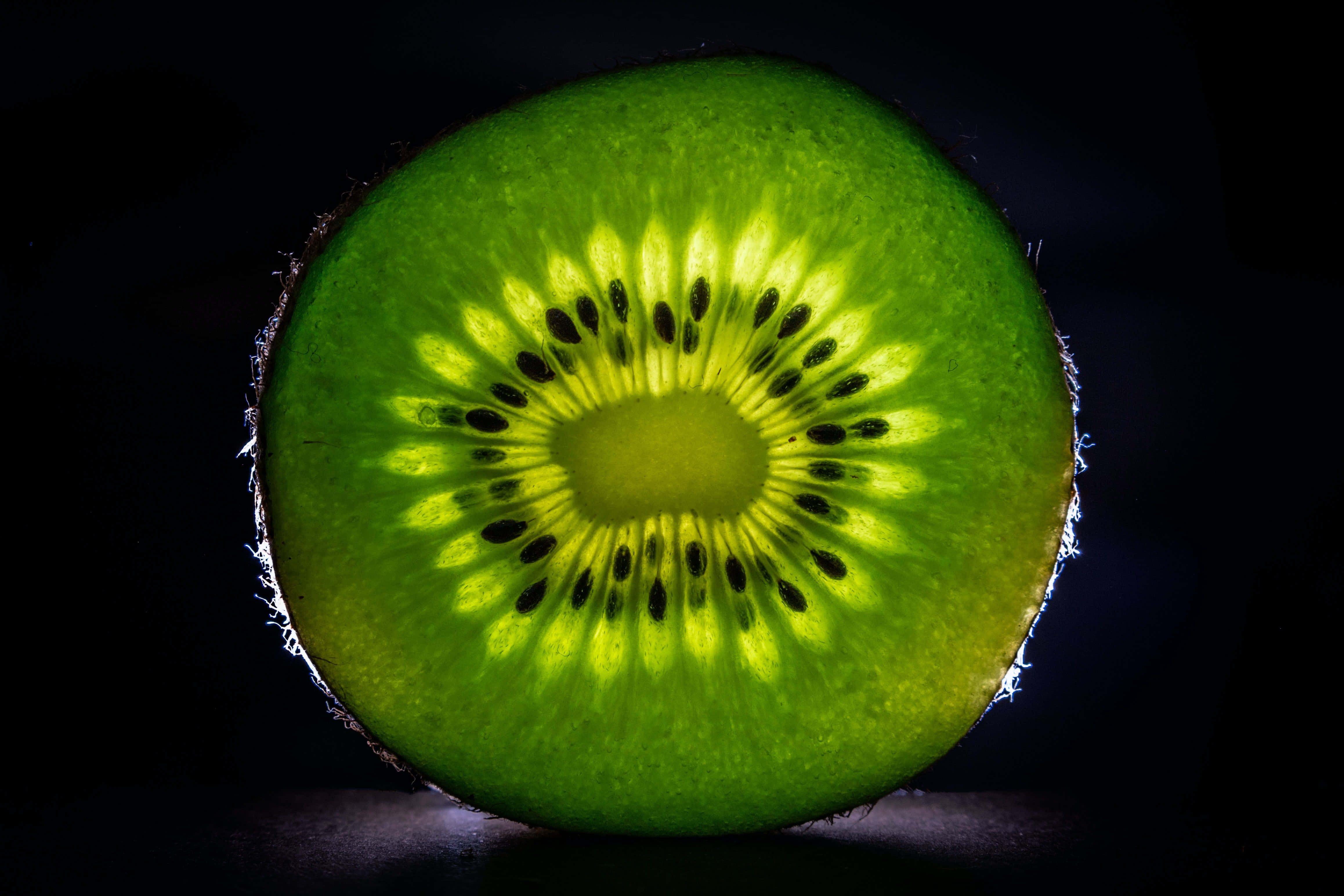 Kiwi 桌布 壁紙 — 一個奇異果的鮮豔橫切面，在深黑色背景下散發出內部光芒。