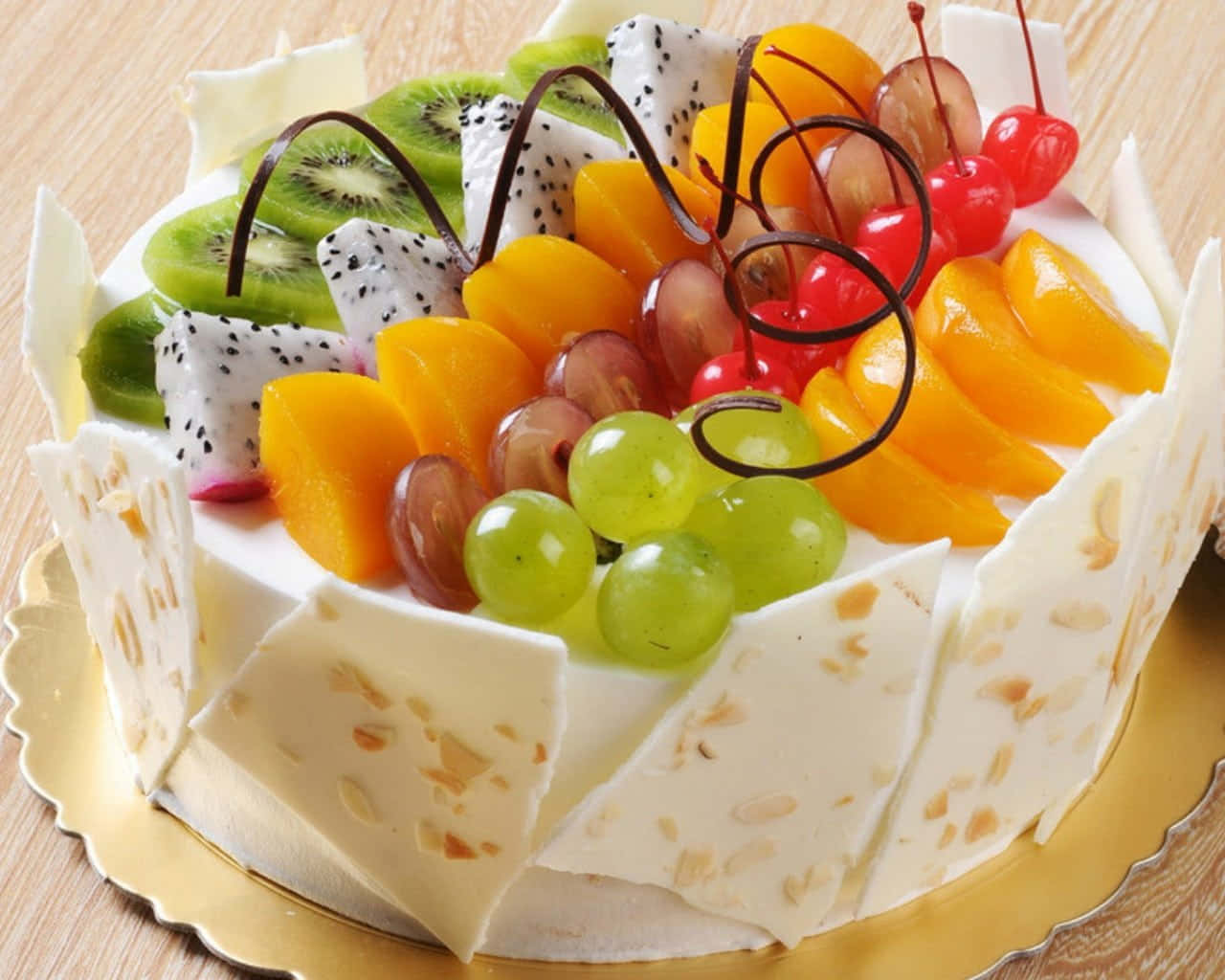 Delightful 桌布 壁紙 — 一個奢華的水果頂層蛋糕，飾以奇異果、火龍果、葡萄、車厘子和橙片，放在金色碟子上。
