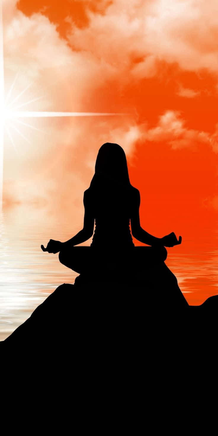 Spiritual Meditation 桌布 壁紙 — 一個女人在日落時分盤腿坐在岩石上冥想嘅剪影，天空係充滿活力嘅橙色，下面係平靜嘅水面。