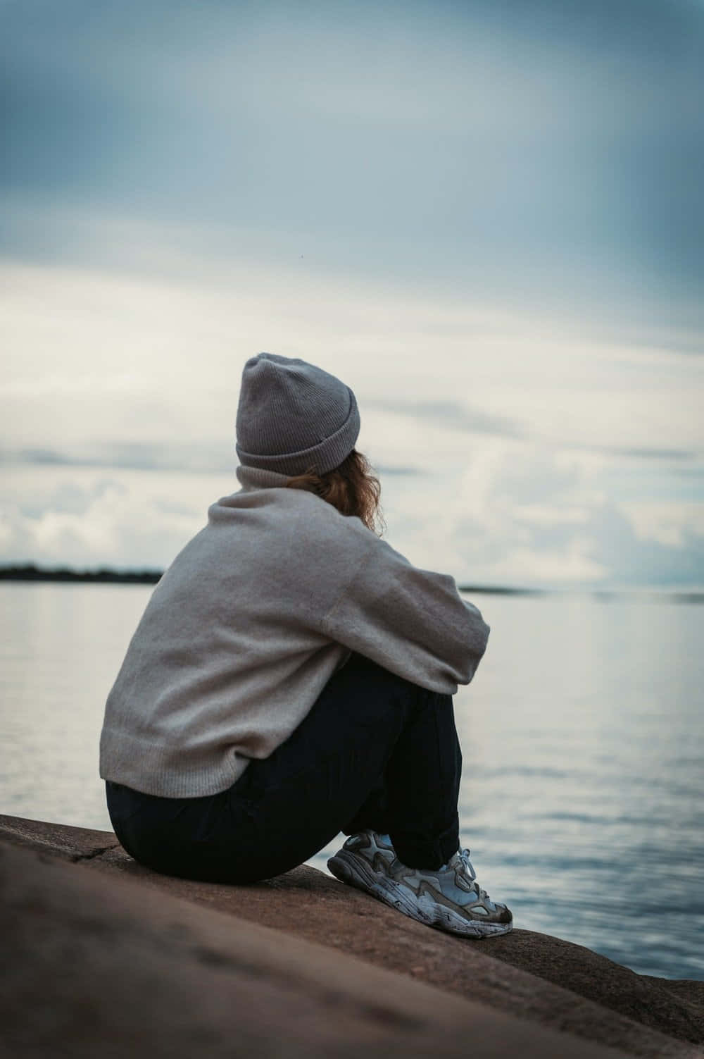 一個女人坐在岩石上望向水面 壁紙