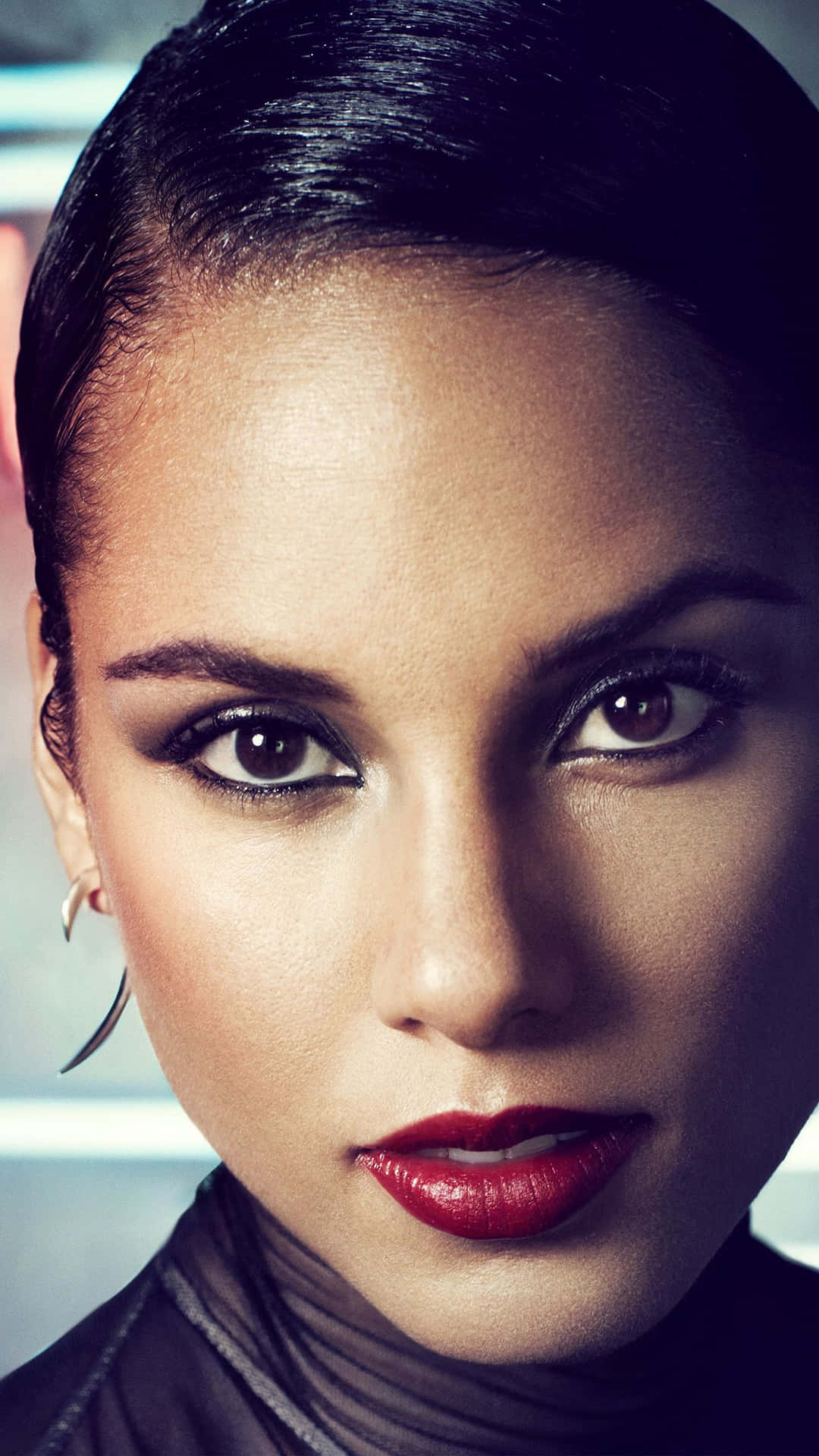 Alicia Keys 桌布 壁紙 — 一個女人的特寫肖像，梳著向後梳的頭髮，大膽的紅唇，在模糊背景下強烈的凝視。