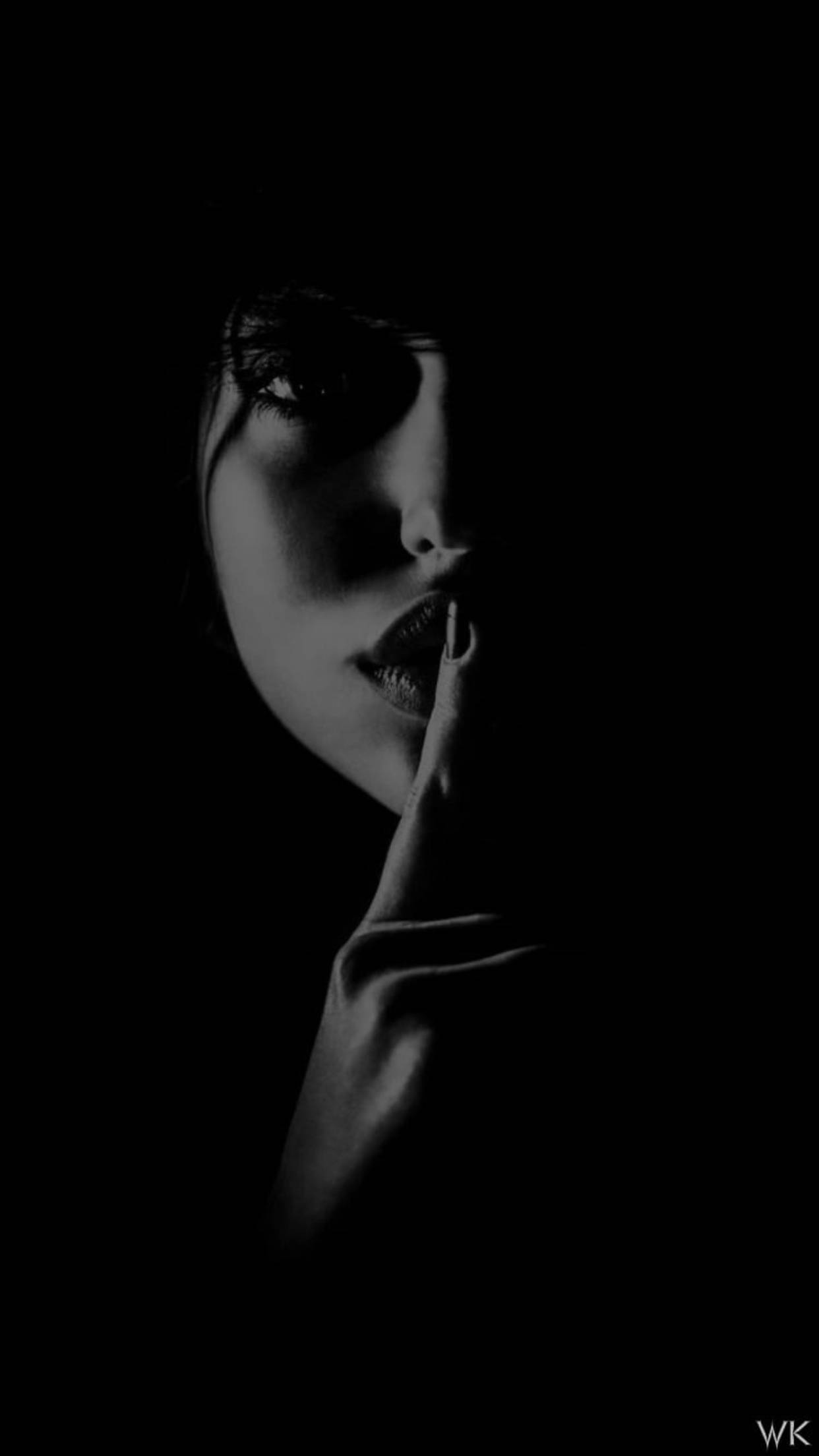 quiet 桌布 壁紙 — 一個女人的臉在陰影中，一根手指按在嘴唇上，做出安靜的手勢，背景為黑色。