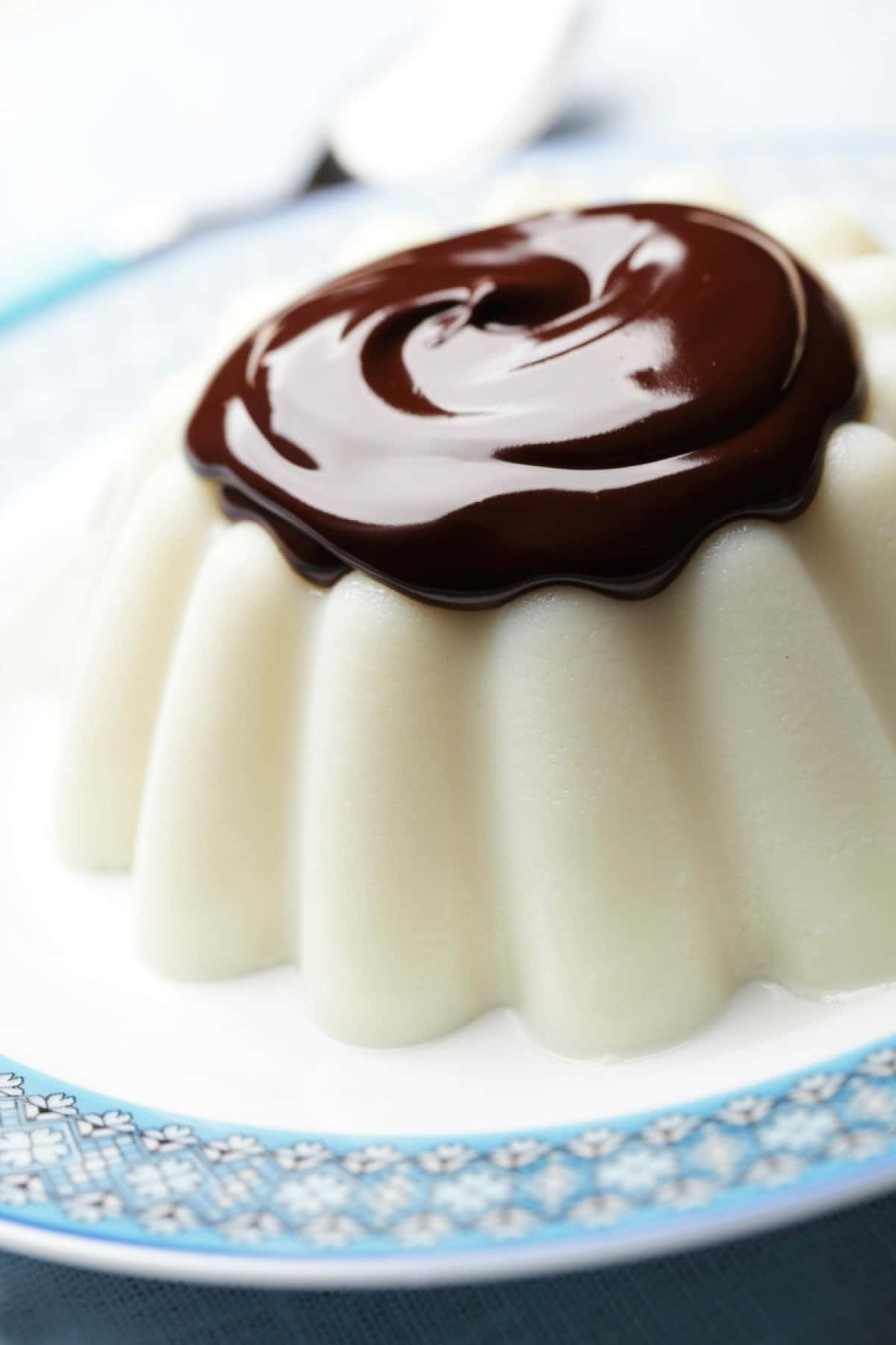Blancmange 桌布 壁紙 — 一個奶油白色法式燉蛋，帶有光澤的深色朱古力漩渦，放在藍色花卉碟上。
