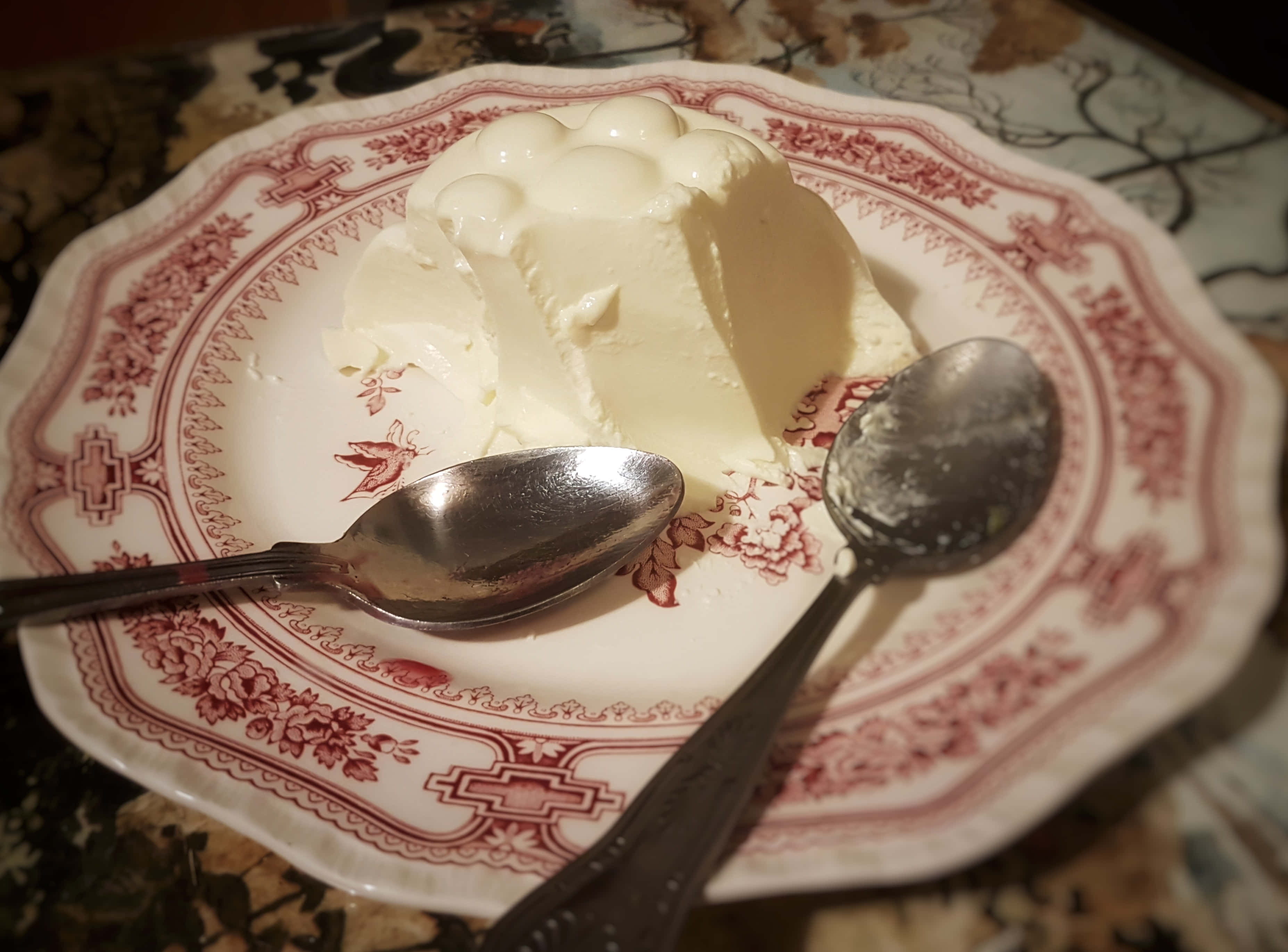 Blancmange 桌布 壁紙 — 一個奶油白色的慕斯優雅地放在復古紅色花卉碟上，旁邊有兩隻湯匙。