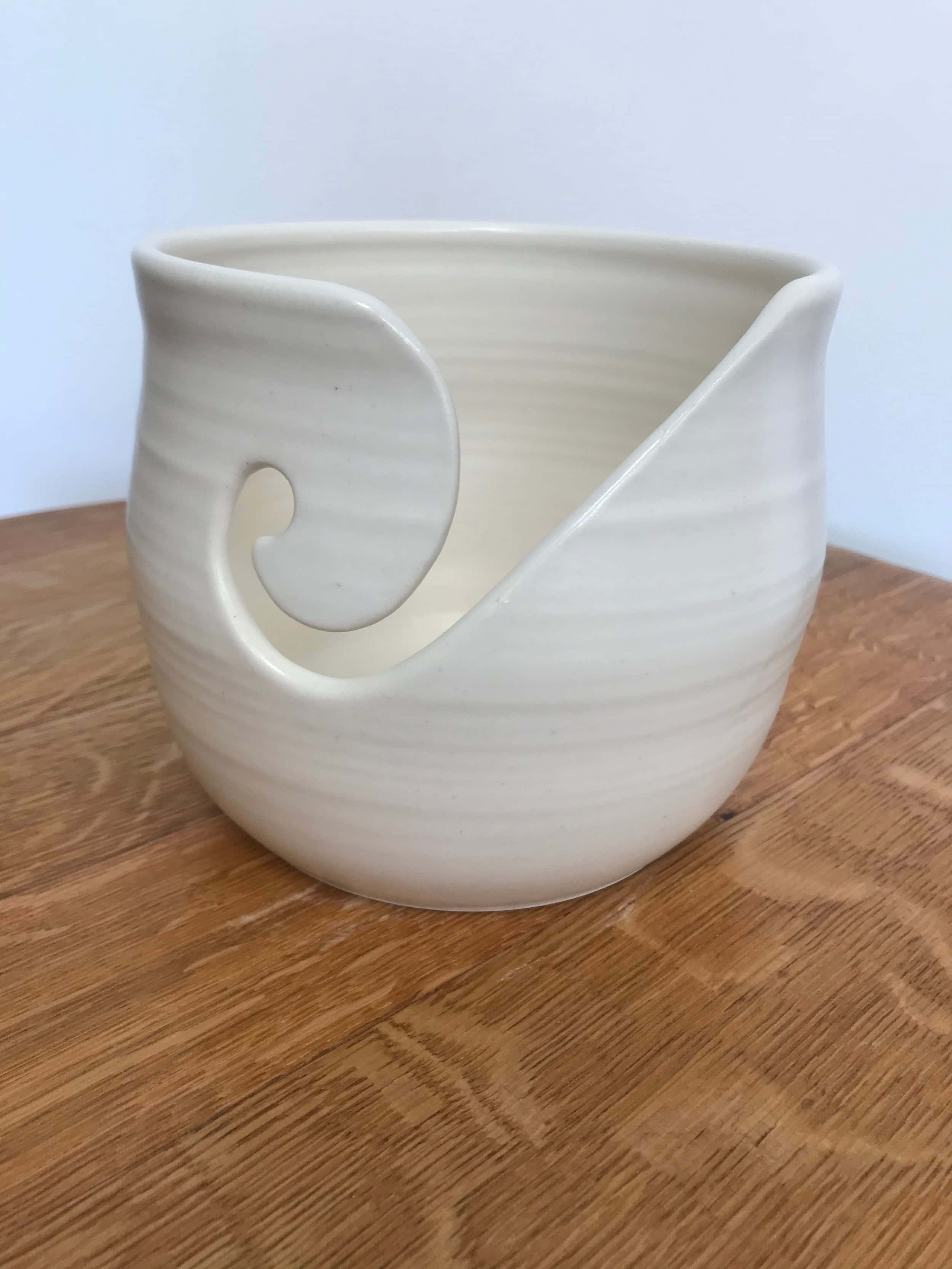 Ceramic 桌布 壁紙 — 一個奶油色陶瓷毛線碗，帶有漩渦手柄，放置在溫暖的木質表面上。