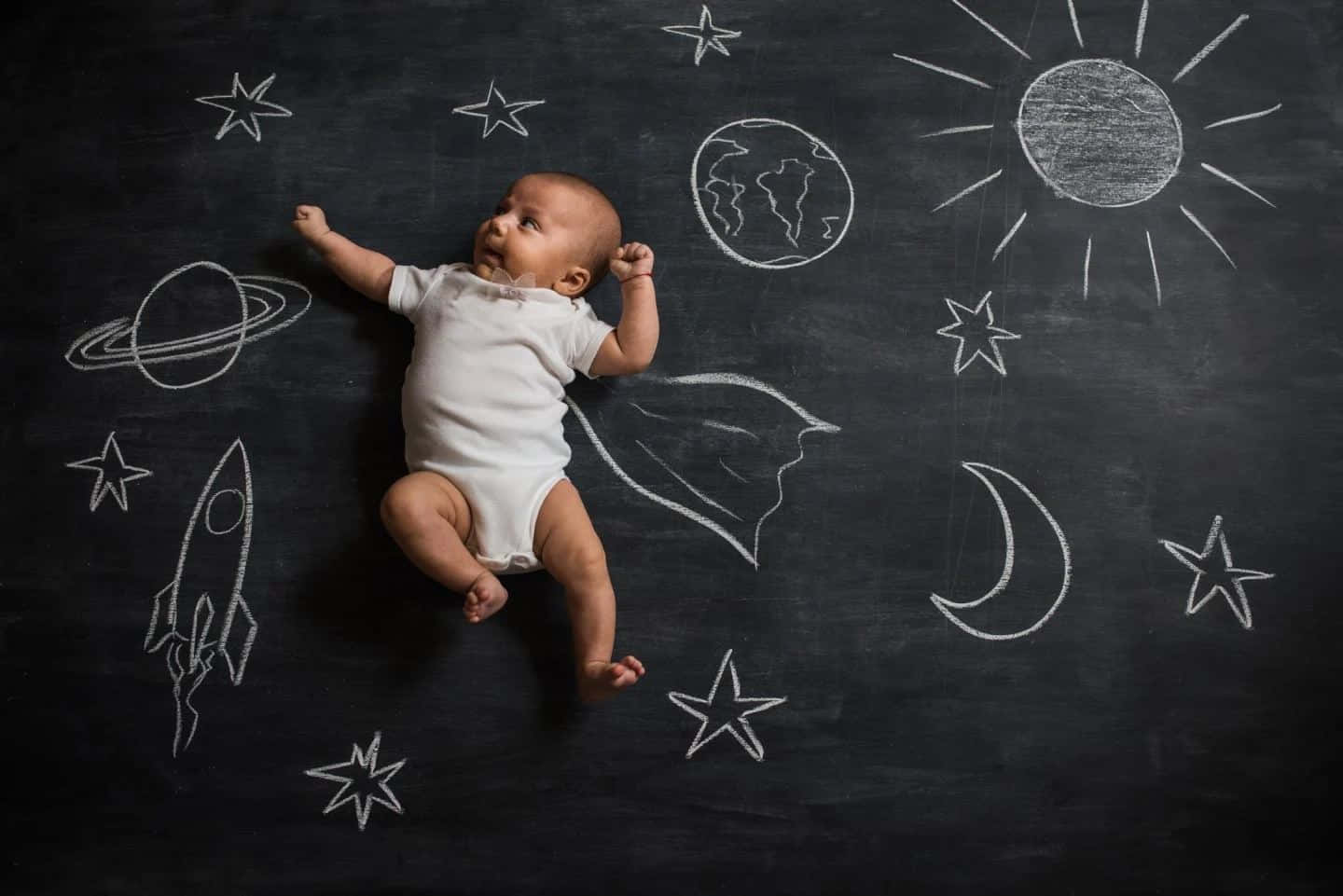 一個嬰兒躺在畫滿星星和行星的黑板上 壁紙