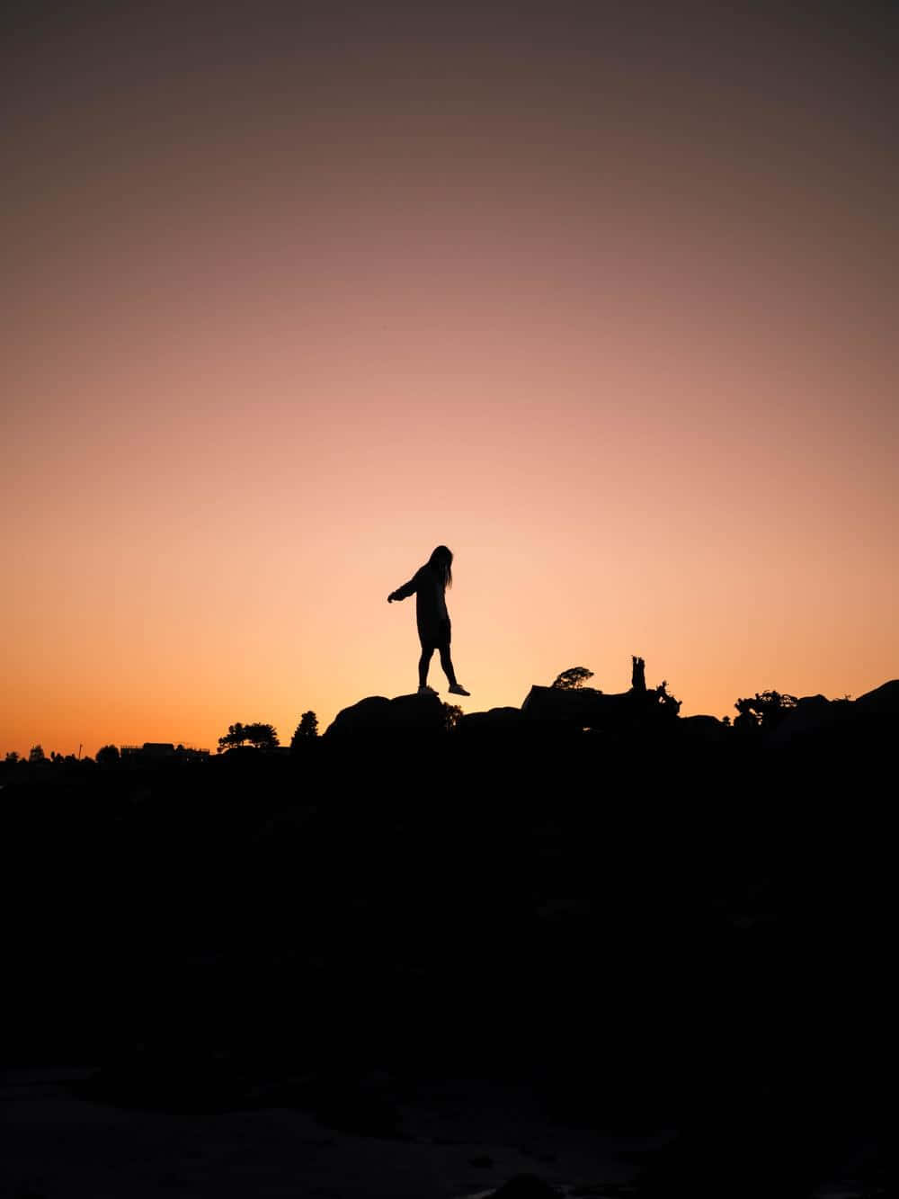 Sunset Silhouette 桌布 壁紙 — 一個孤獨的人影站在岩石露頭上，背景是充滿活力的橙色和紫色日落天空。