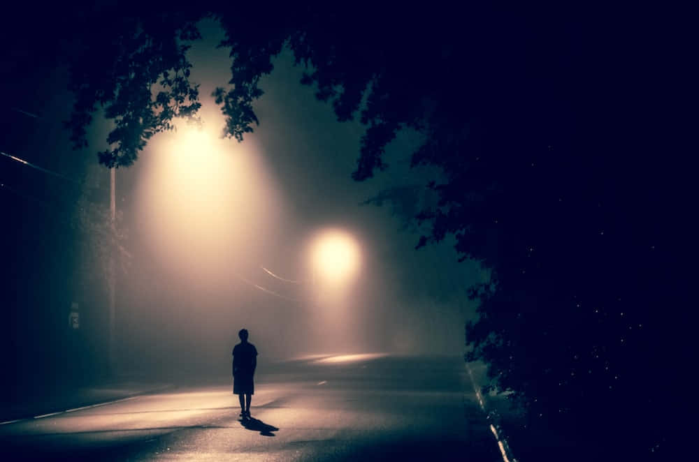 一個人在發光的街燈下，獨自走在霧濛濛的夜街上。