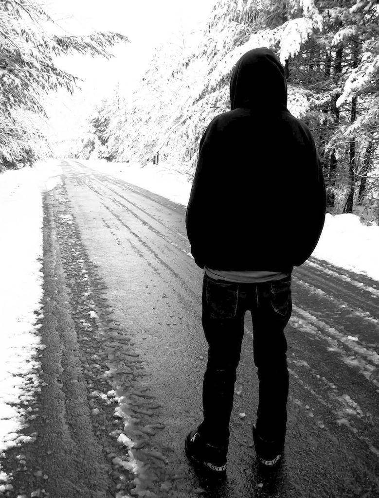 emo 桌布 壁紙 — 一個孤獨的戴帽人影站在冬季森林的積雪道路上，背對鏡頭，呈現鮮明的黑白對比。