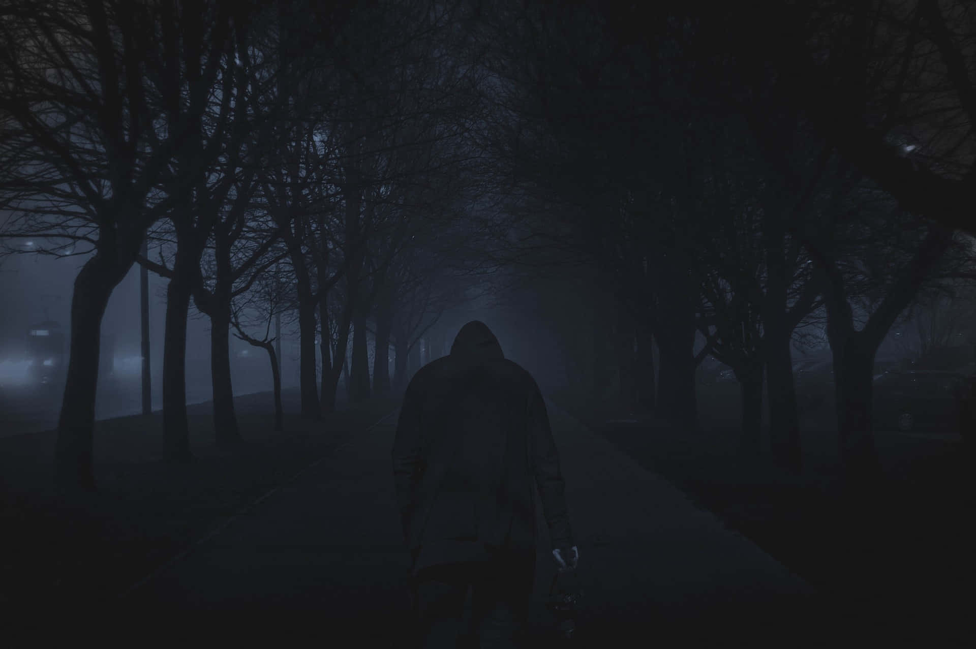 Dark Road 桌布 壁紙 — 一個孤獨的戴帽身影在黑暗夜空下，沿著一條霧氣瀰漫、樹木成蔭的小徑行走。