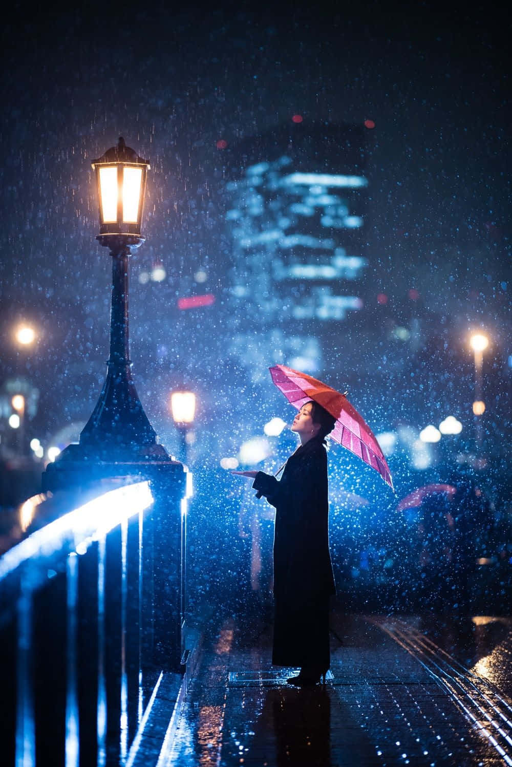 鎖屏 桌布 壁紙 — 一個孤獨的身影在夜間城市橋樑上，在閃爍街燈照耀下，撐著粉紅色雨傘站在雨中。