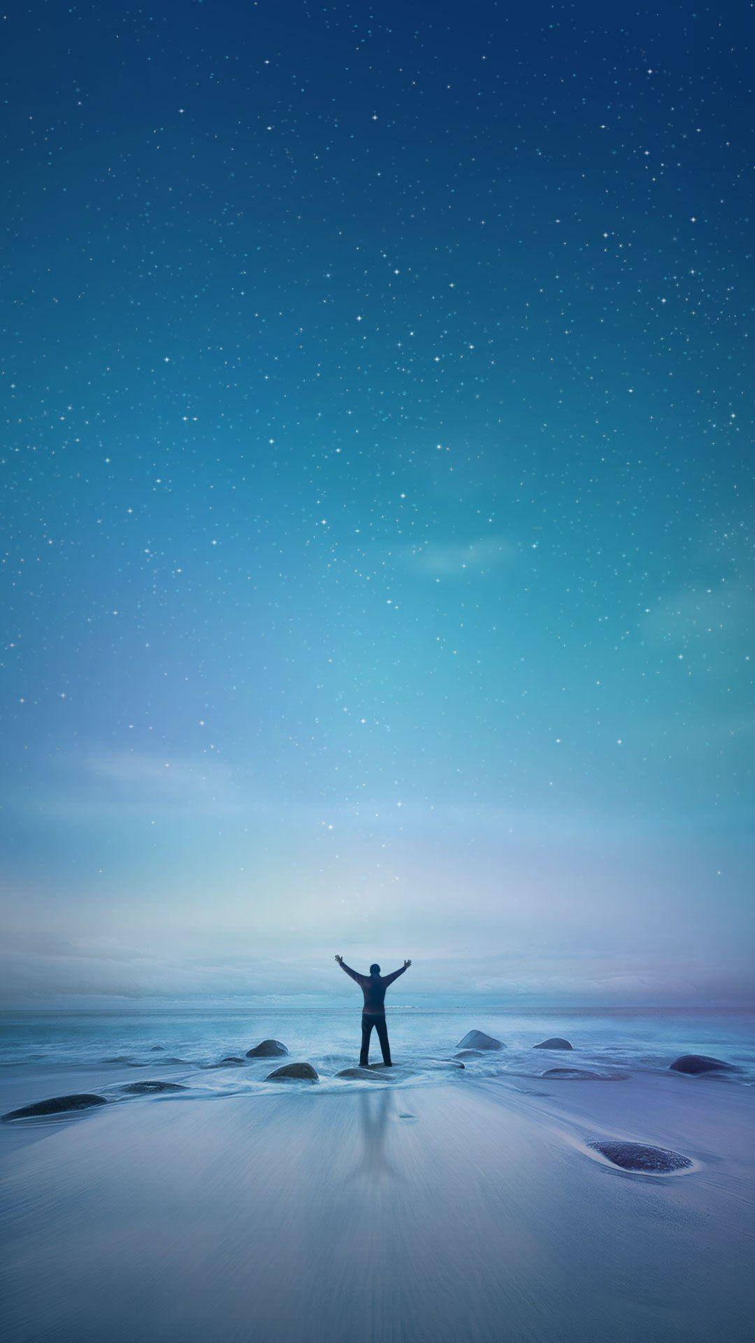 人在海灘上高舉雙臂，背景是繁星點點的暮色天空