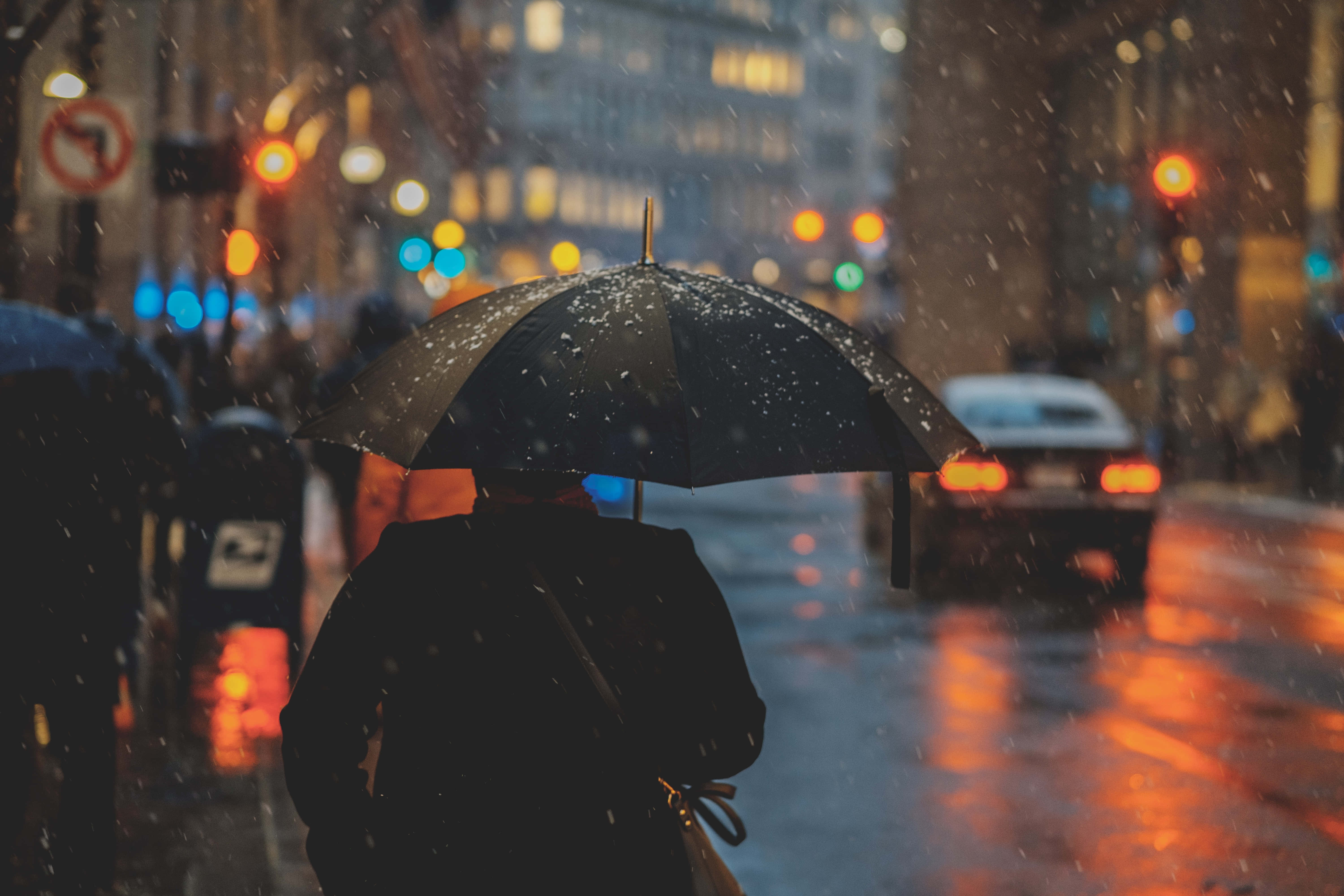 男人 桌布 壁紙 — 一個孤獨的身影在雨夜的街道上行走，手持黑色雨傘，濕漉漉的人行道反射著溫暖的街燈。