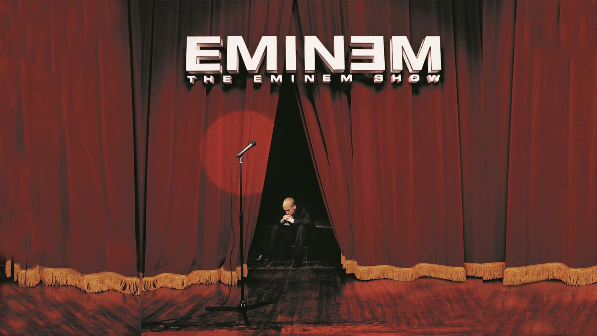 Eminem 桌布 壁紙 — 一個孤獨的身影坐在舞台上，紅色帷幕下，有咪高峰和上方 'Eminem The Eminem Show' 文字。