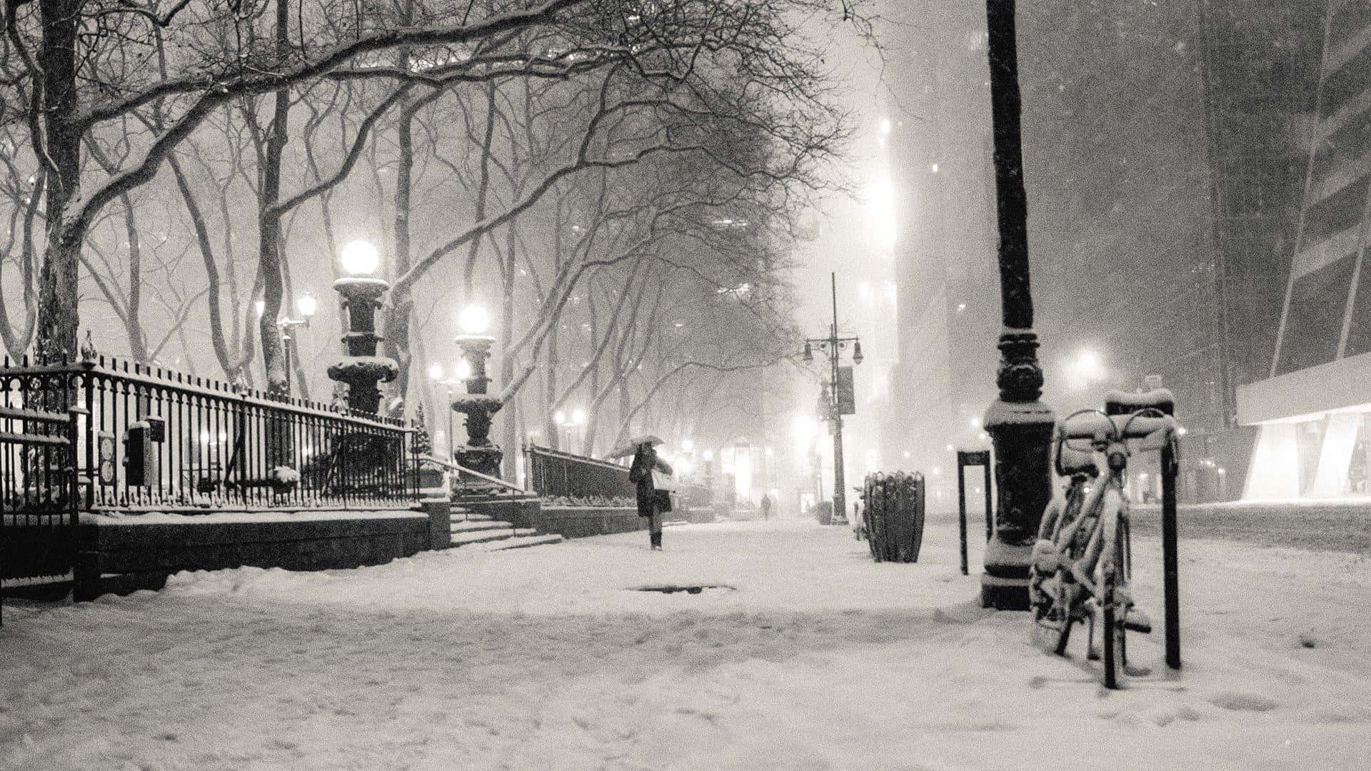 Winter Cityscape 桌布 壁紙 — 一個孤獨的身影撐著傘，走在白雪覆蓋的城市人行道上，兩旁是光禿禿的樹木和發光的街燈。