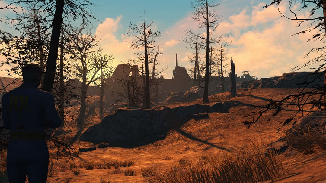Fallout 4 The Capital Wasteland 桌布 壁紙 — 一個孤獨的身影穿著藍色避難所連身衣，站在夕陽下的荒蕪廢土中，凝視著廢棄的建築和光禿的樹木。