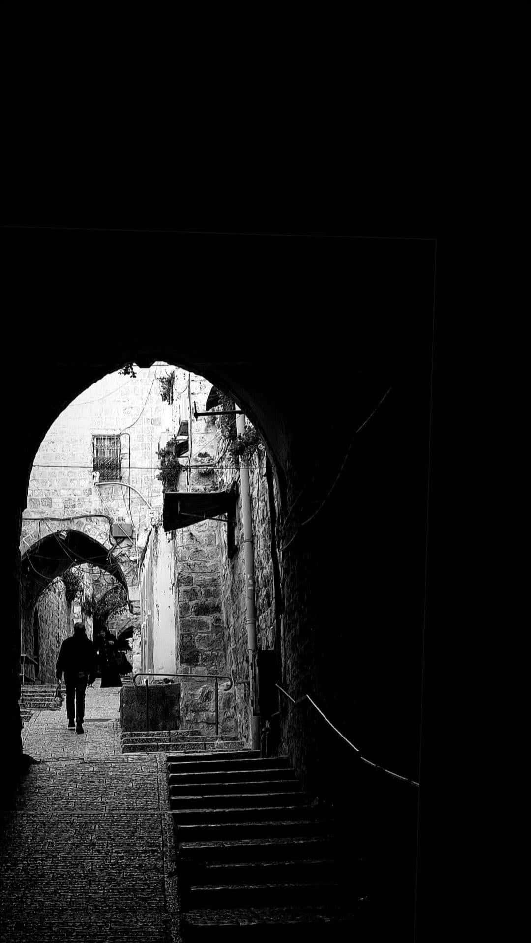 Palestine 桌布 壁紙 — 一個孤獨的身影穿過陰暗的石拱門，走進陽光普照的古老小巷。