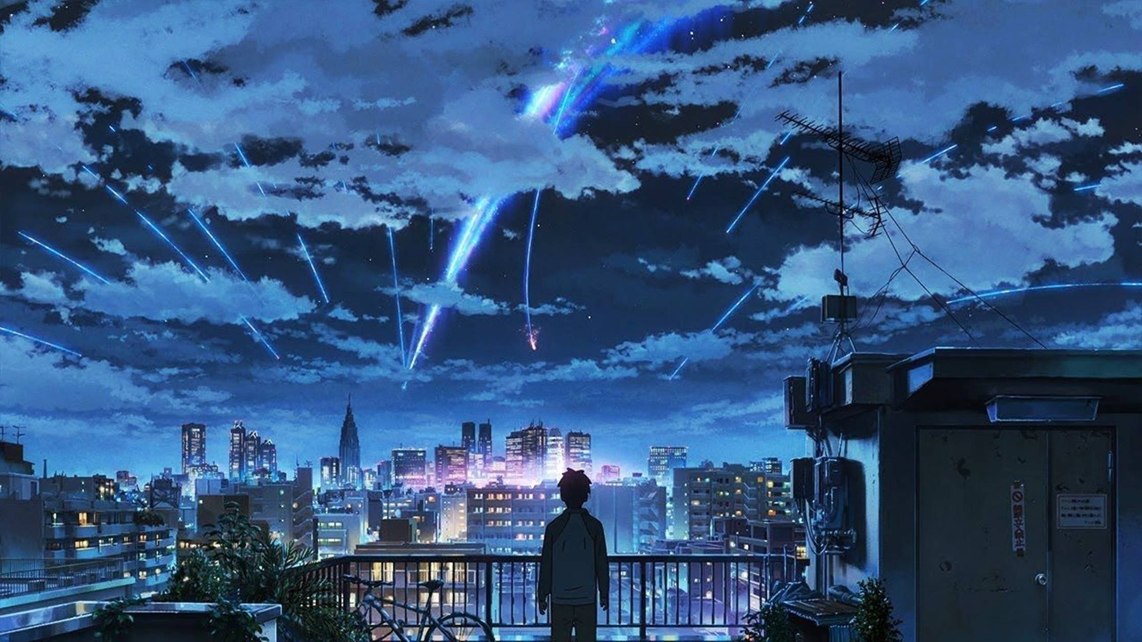 動漫男孩 桌布 壁紙 — 一個孤獨的身影站在屋頂陽台上，凝視著下方充滿活力的城市景觀，藍色光線穿過多雲的夜空如雨般落下。