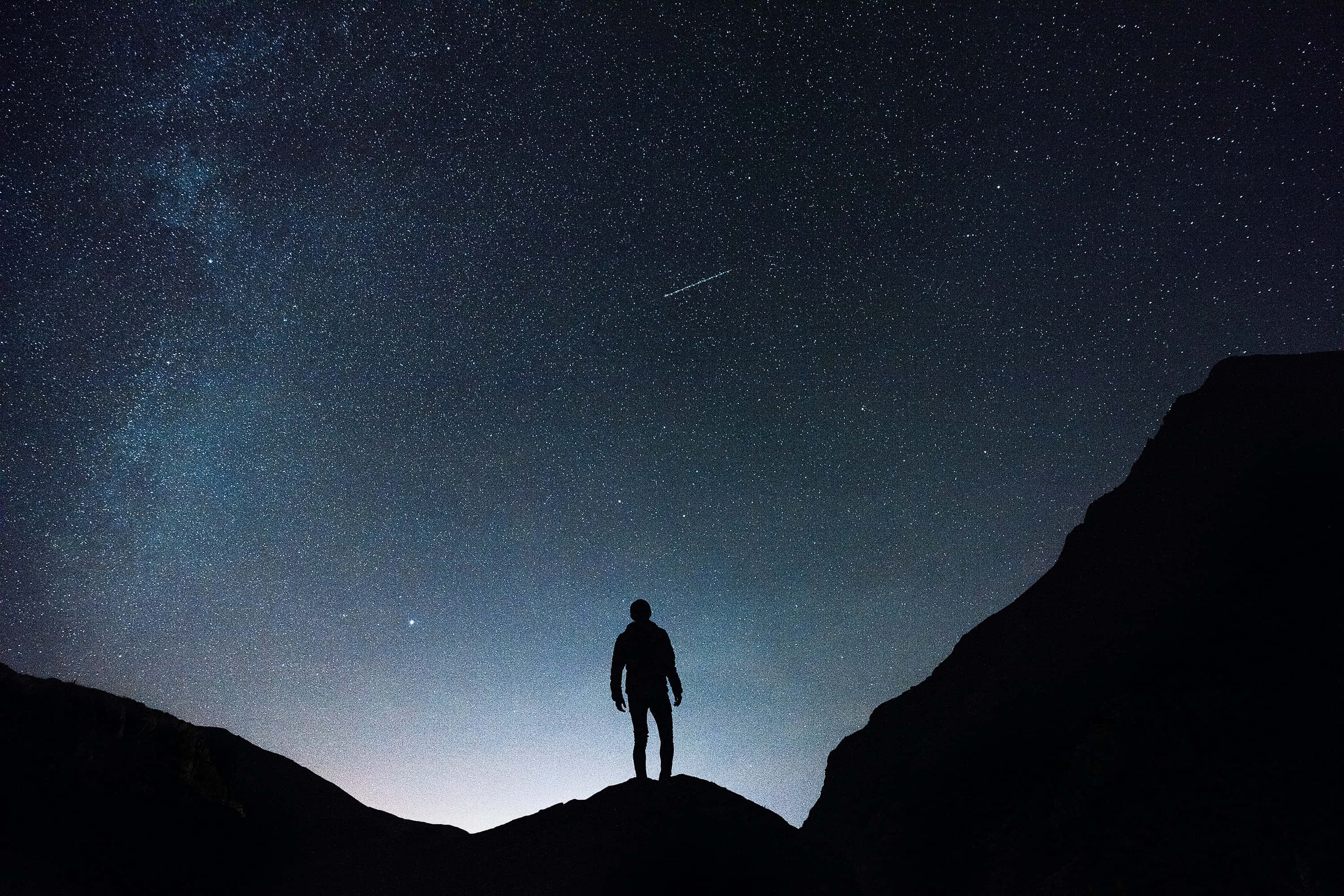 Silhouette 桌布 壁紙 — 一個孤獨的身影站在山脊上，下方是令人嘆為觀止的星空，有銀河和流星。