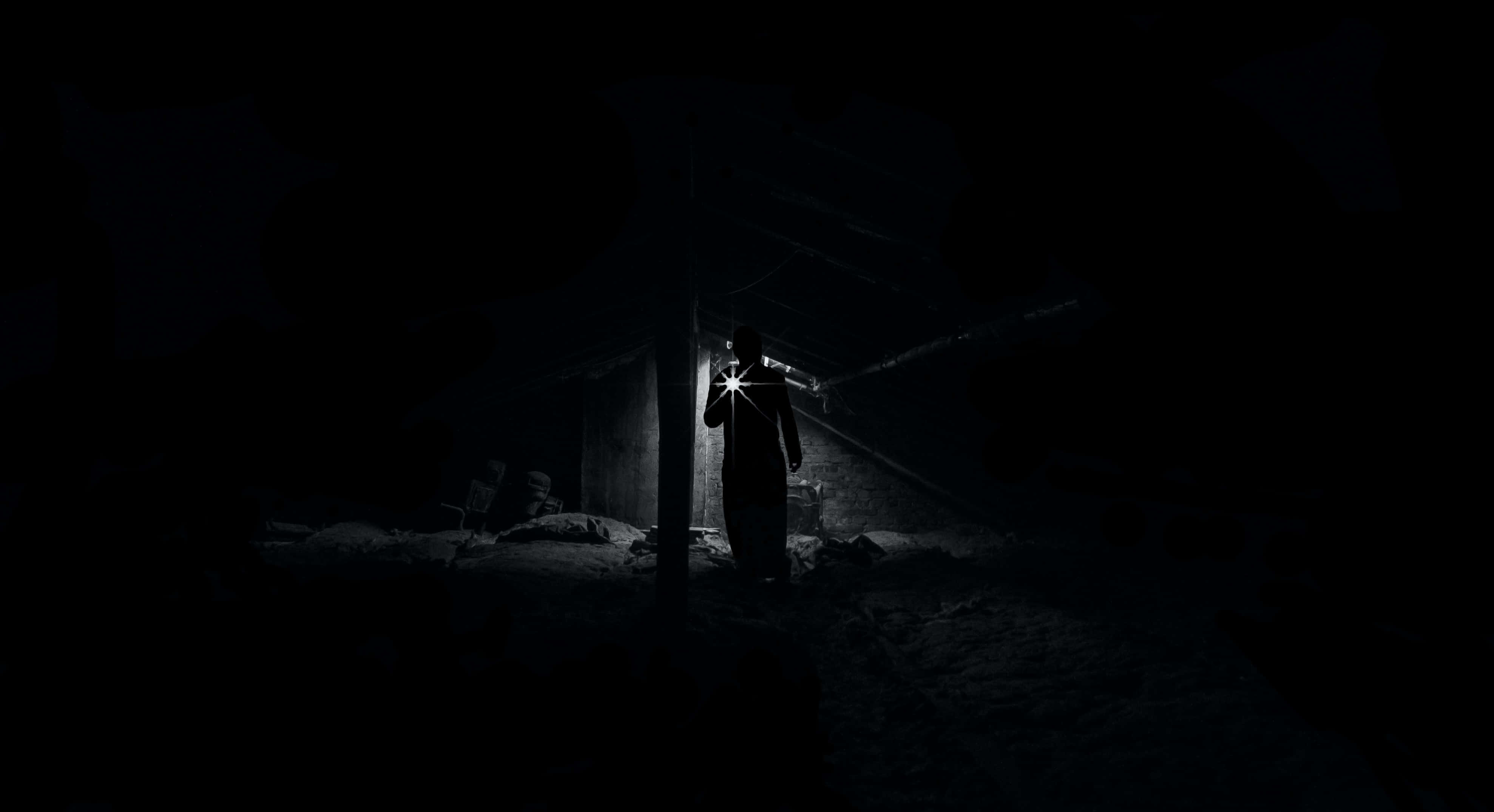 Dark Fear 桌布 壁紙 — 一個孤獨的身影站在漆黑的廢墟中，手持電筒劃破黑暗，照亮灰塵和瓦礫。