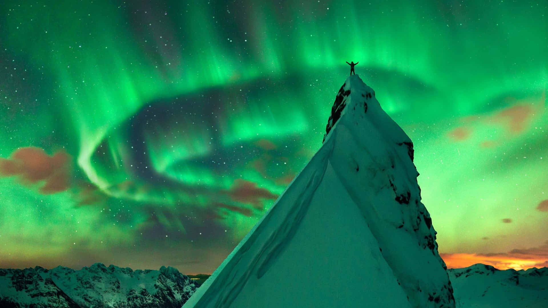 aurora borealis 桌布 壁紙 — 一個孤獨的身影站在白雪覆蓋的山峰頂上，下方是充滿活力的綠色北極光在繁星點點的暮色天空中旋轉。